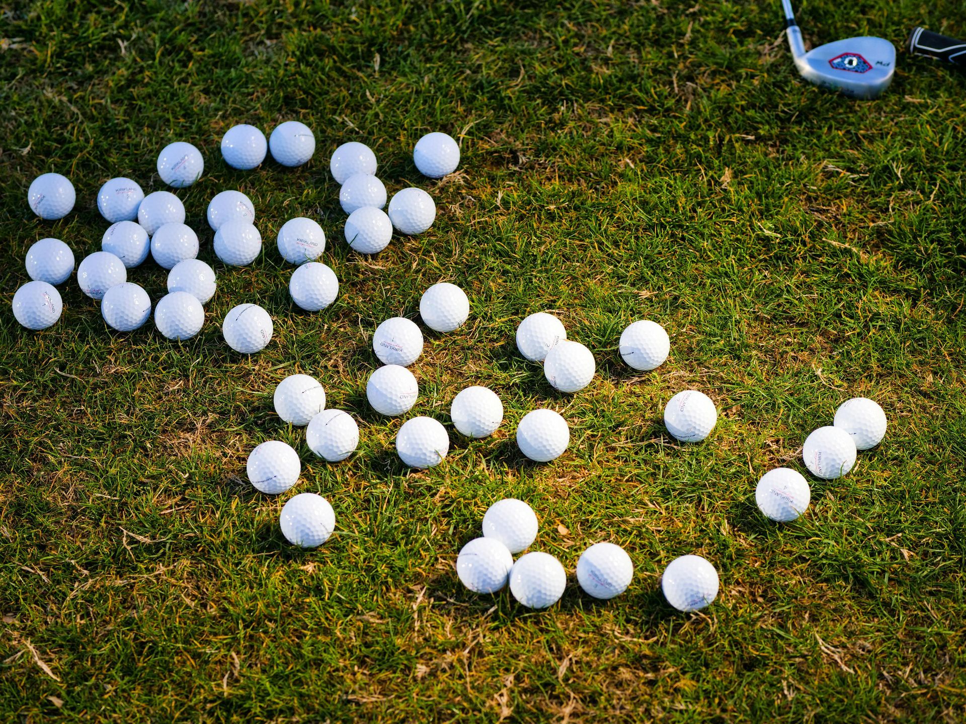 Golf balls scattered on green grass near a golf club.