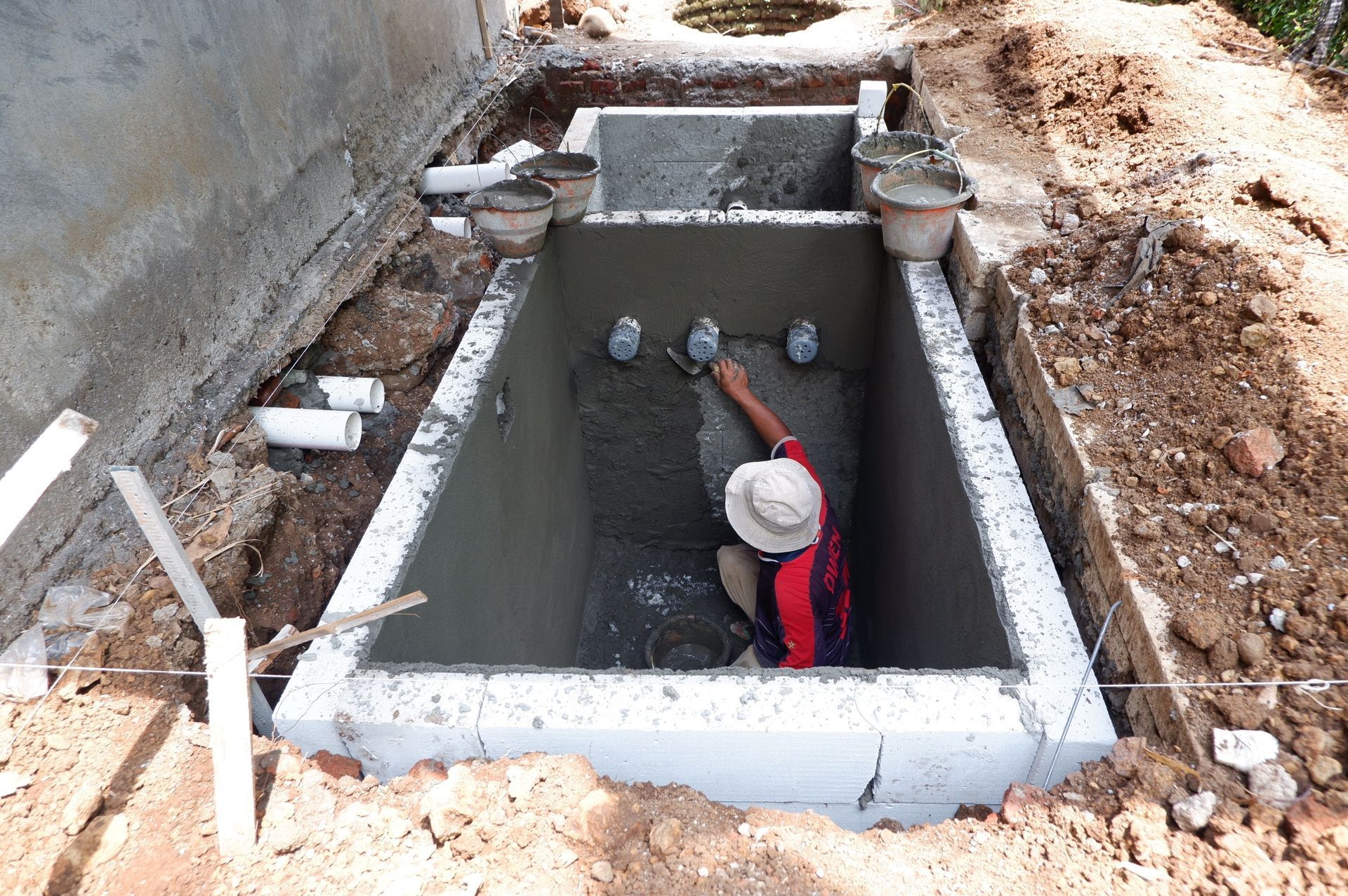 Worker in a concrete pit, reaching up toward pipes during underground utility construction.