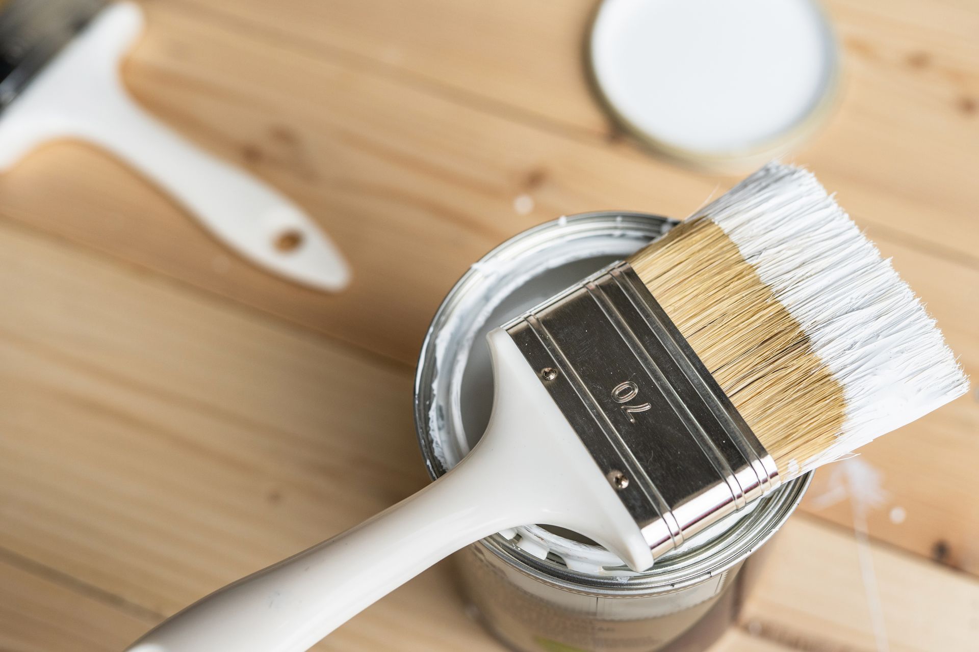 A paint brush is sitting in a can of paint on a wooden table.