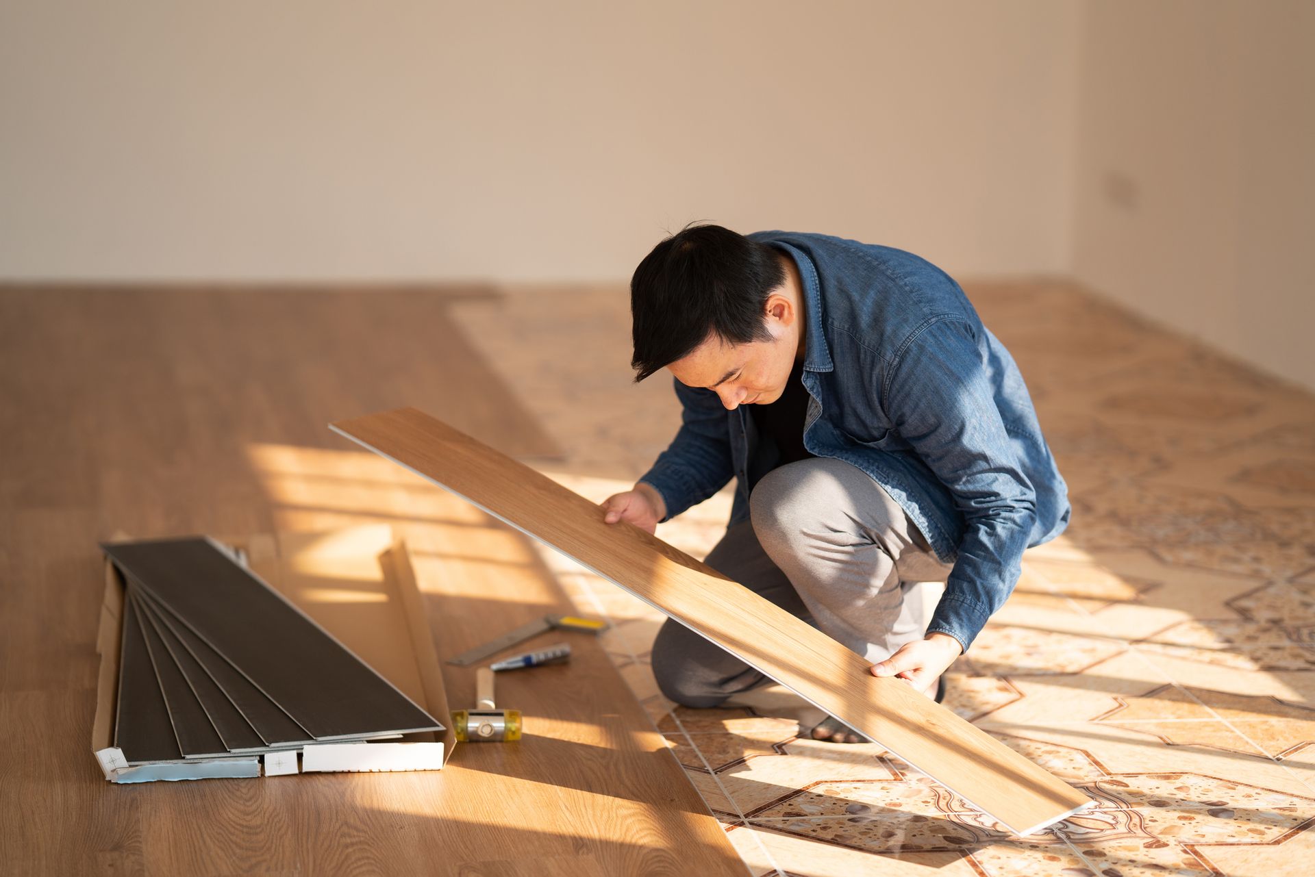 A man is kneeling down to install a wooden floor.
