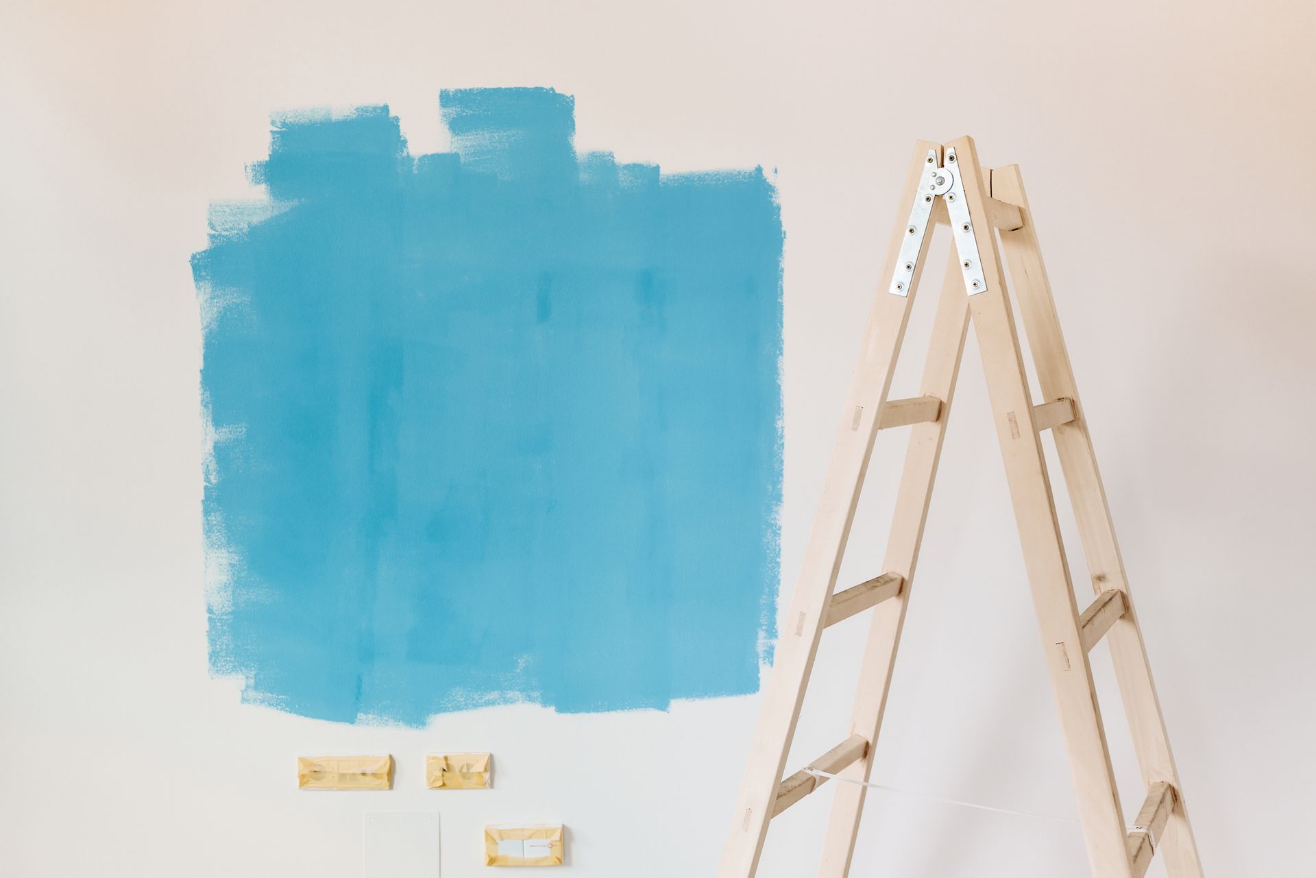 A wooden ladder is sitting next to a blue painted wall.