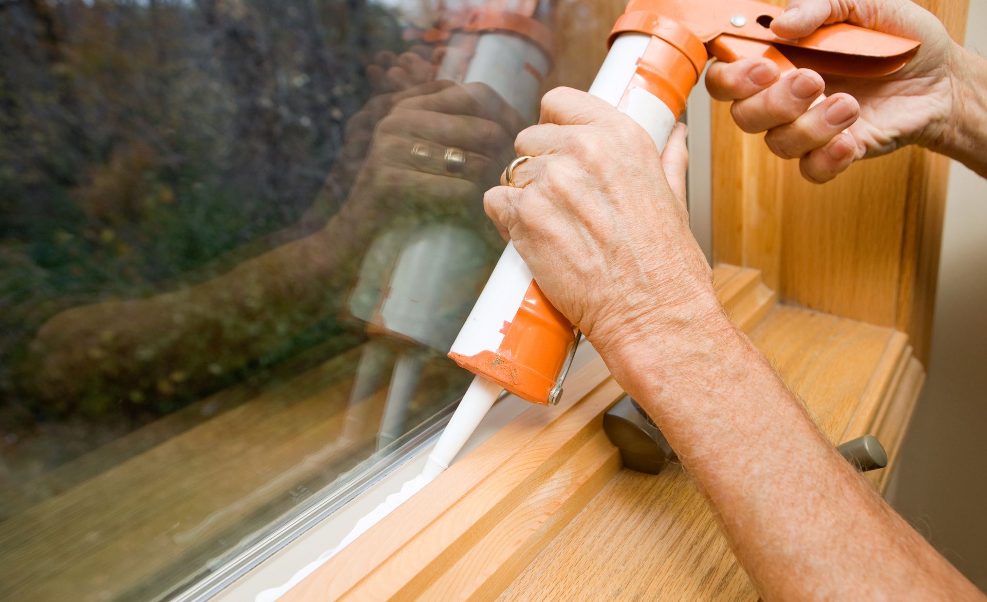 A person is applying silicone to a window sill.