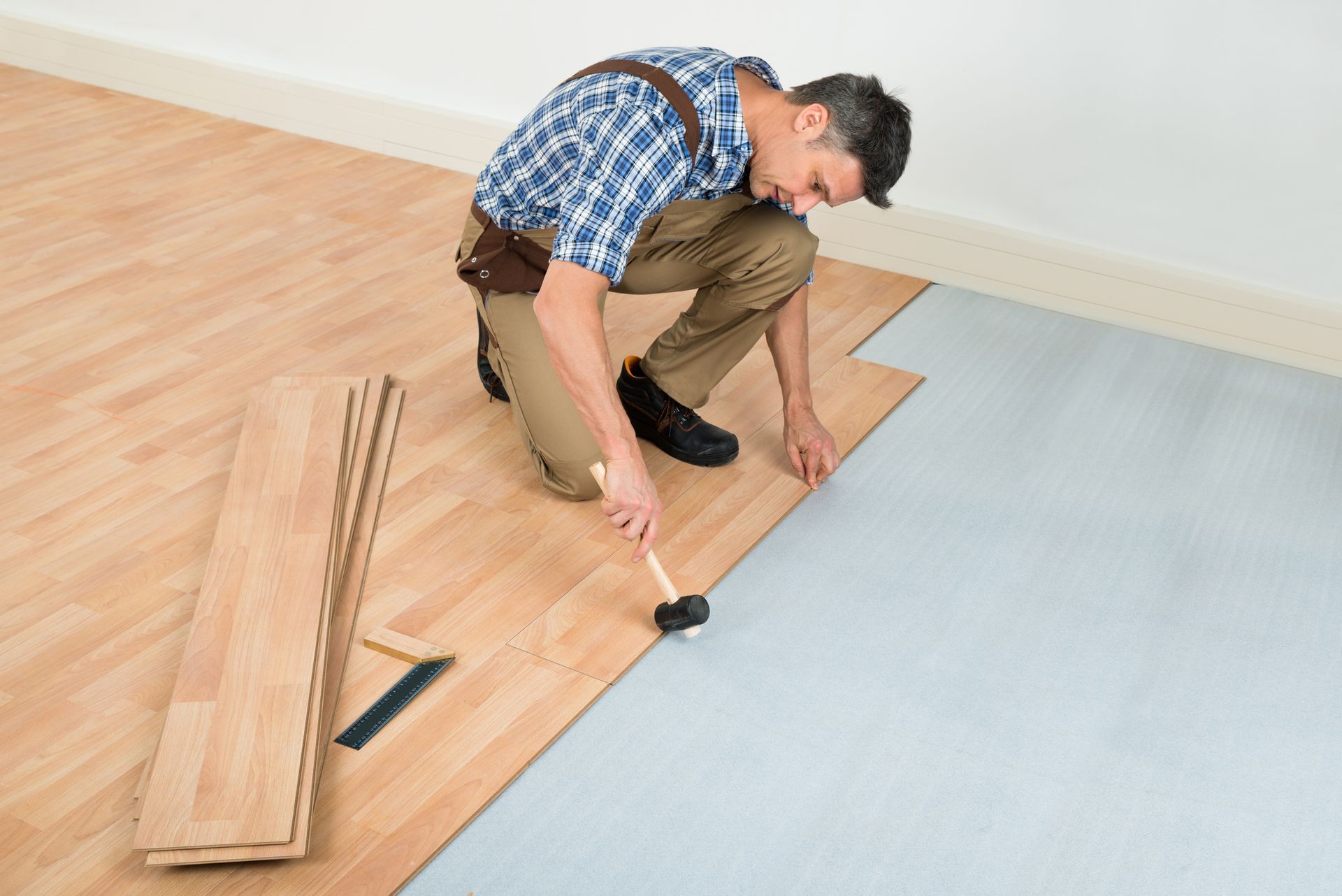 A man is installing a wooden floor with a hammer.