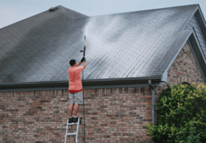 man standing on ladder soft washing roof in springdale arkansas