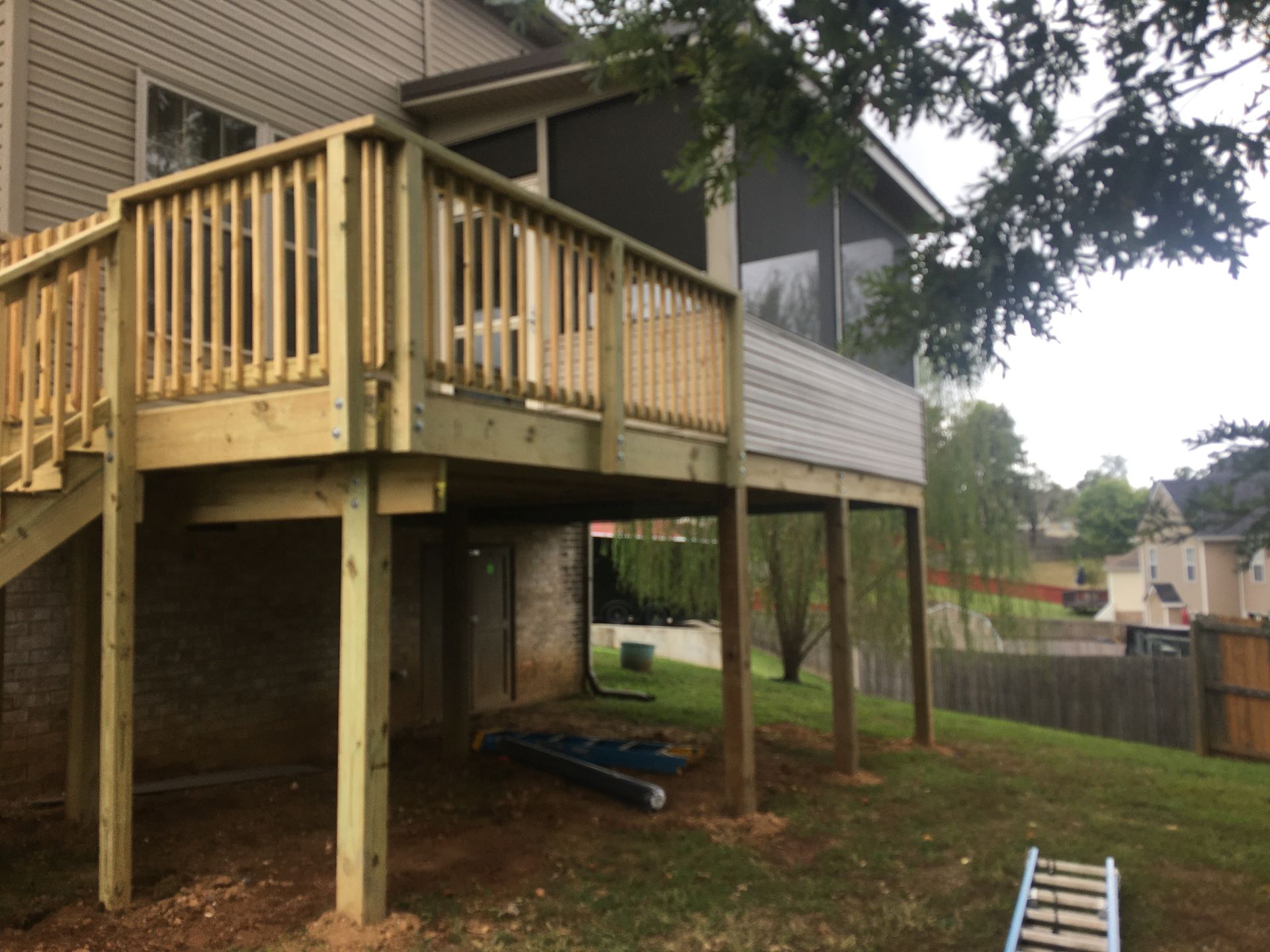 Wooden deck attached to a house with a screened porch, overlooking a grassy backyard.