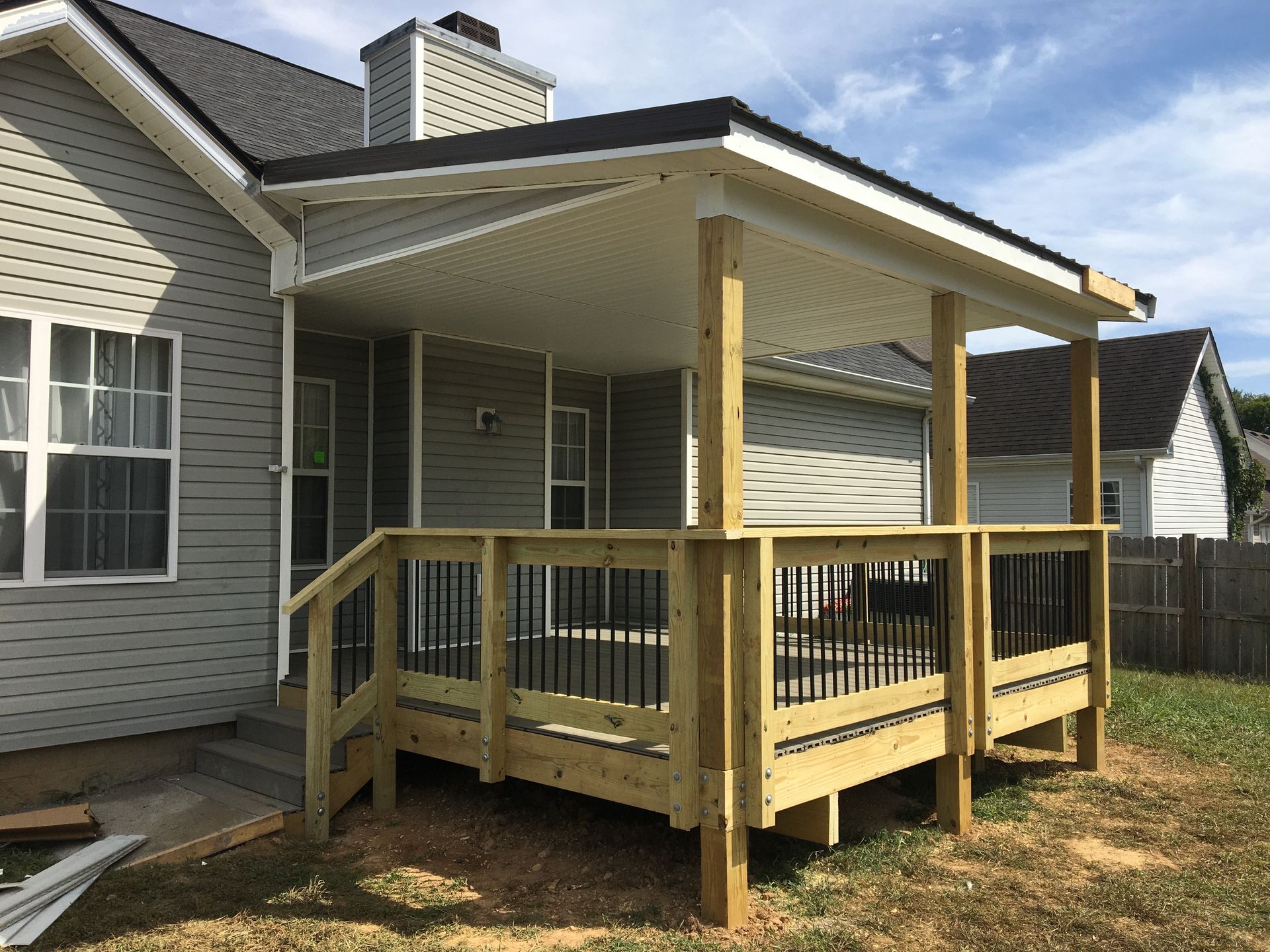 A new wooden deck with a covered roof attached to a light gray house.
