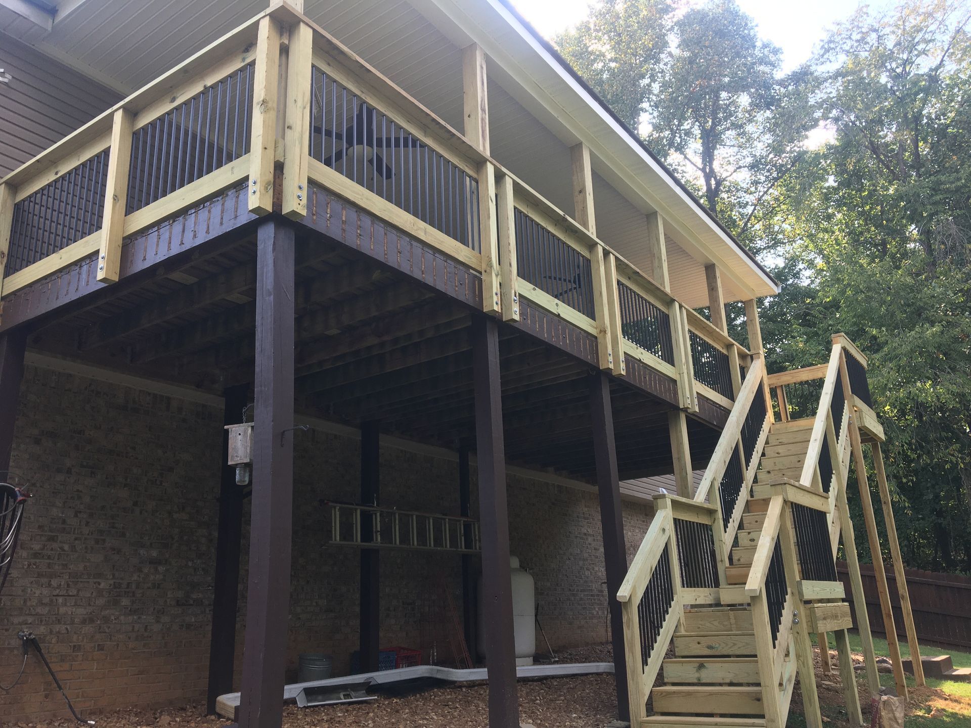 Two-story deck with stairs. Brown posts and railing; gray deck boards; light wood stairs.