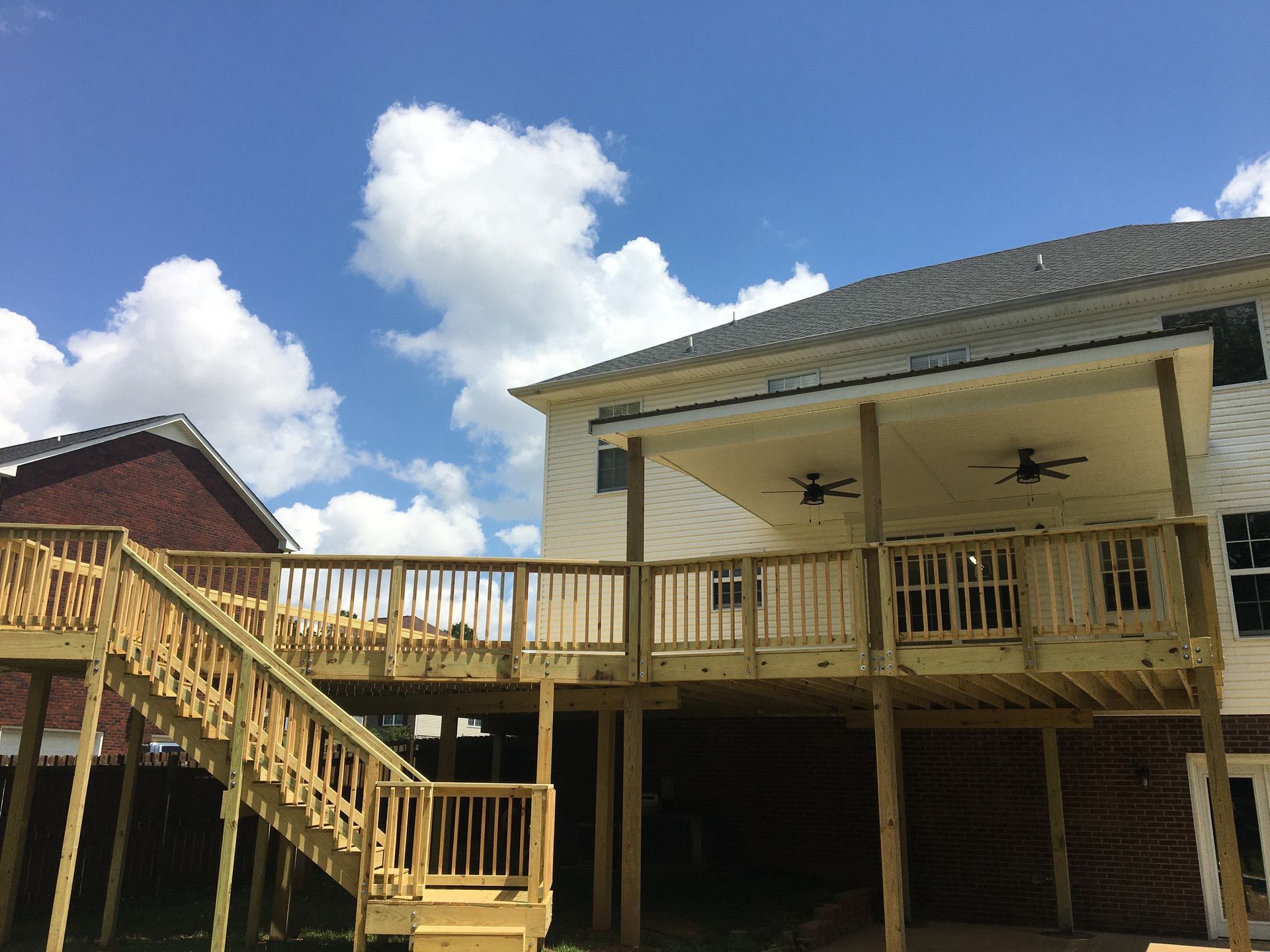 Wooden deck and stairs attached to a house with a covered porch, blue sky in the background.