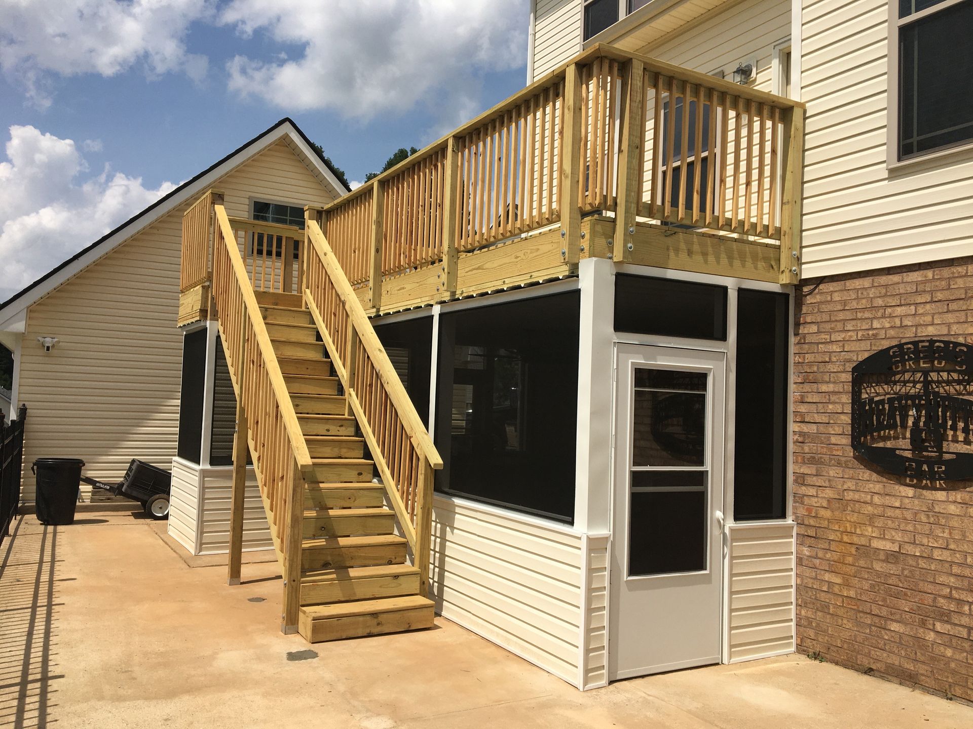 Wooden deck with stairs leading to a screened-in porch next to a house.