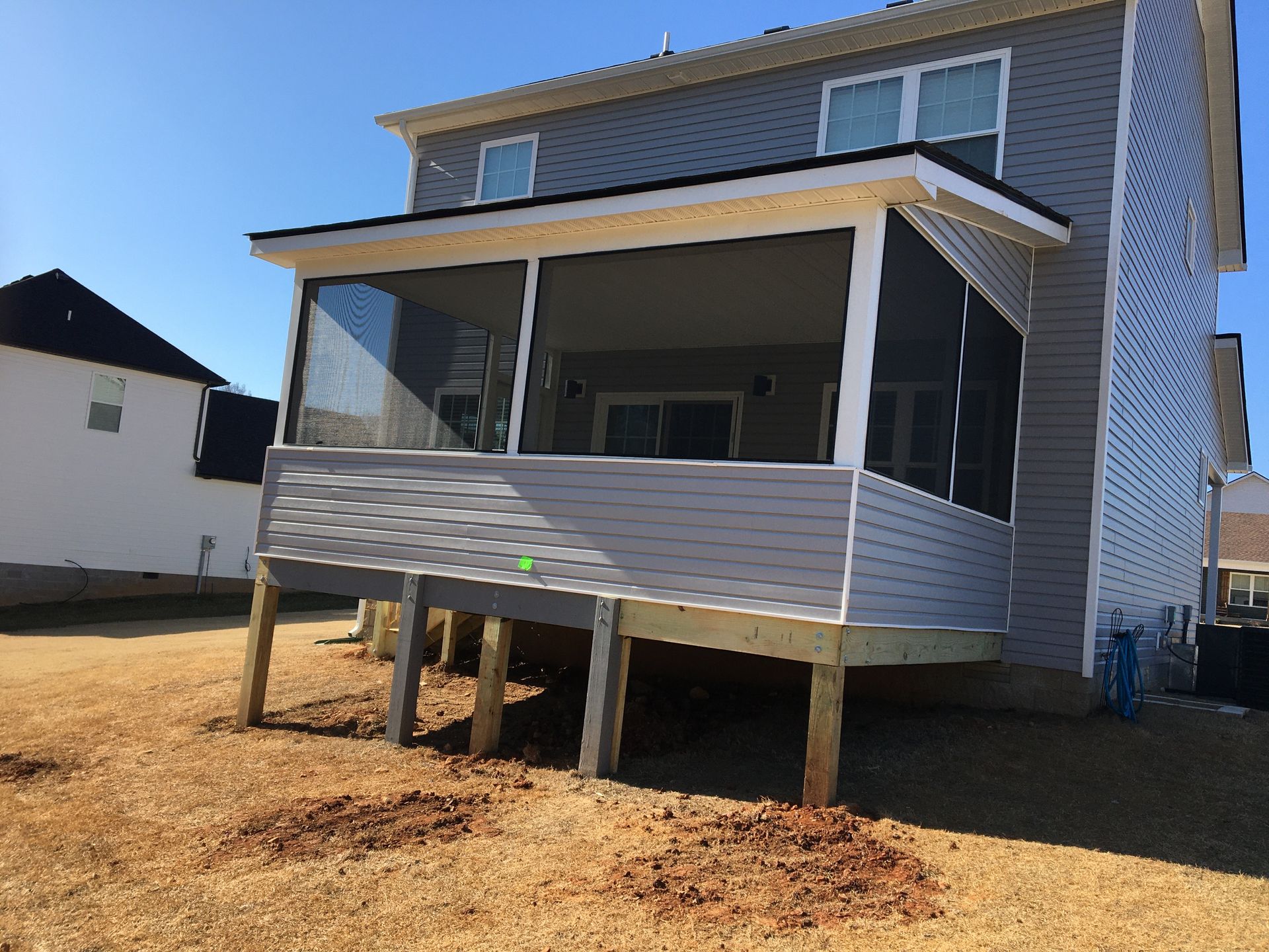 A two-story house with a screened porch on a raised wooden deck, set in a yard with dry grass.