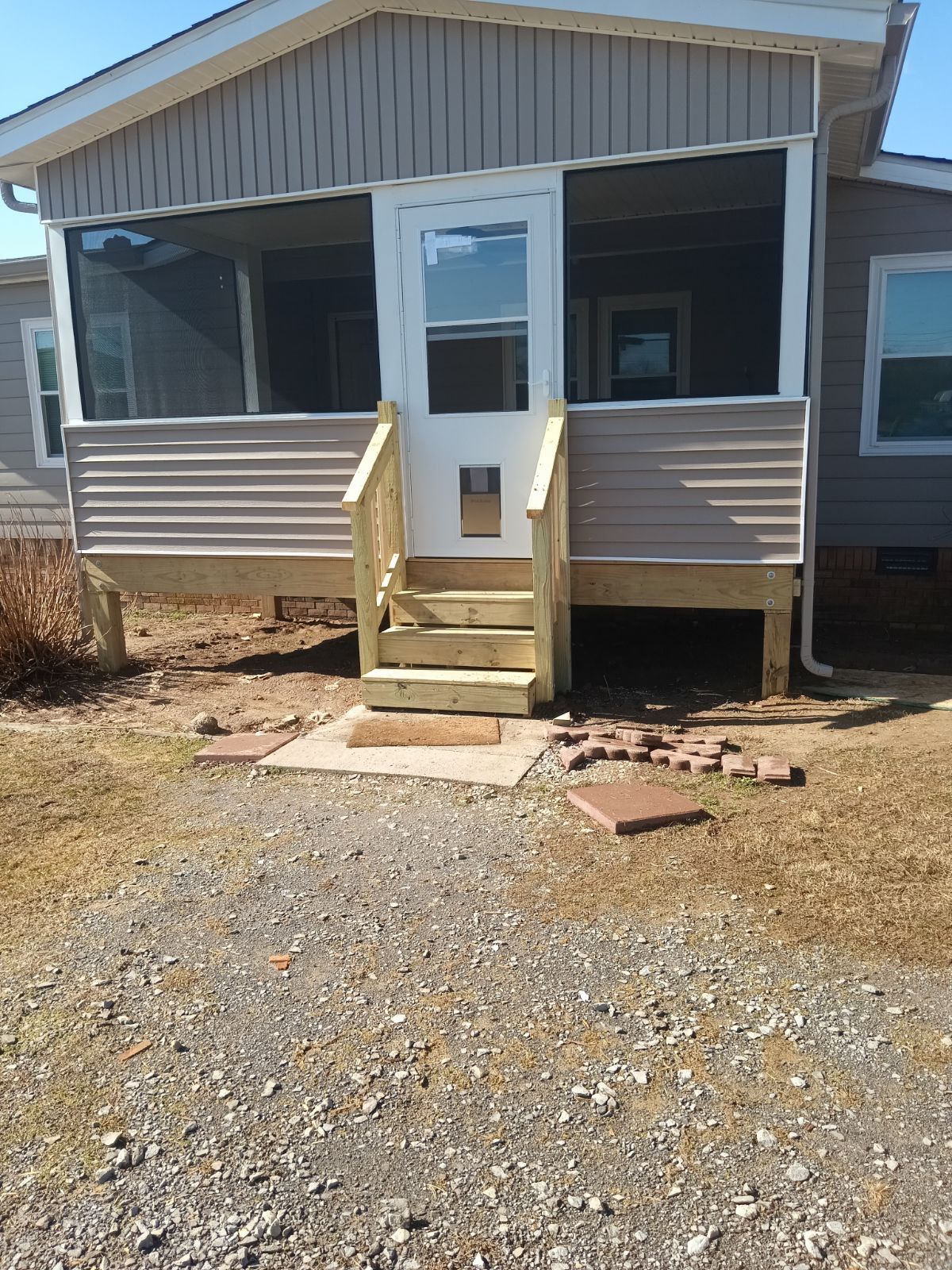 A house with a screened-in porch and wooden steps leading to a white door. The facade is tan.