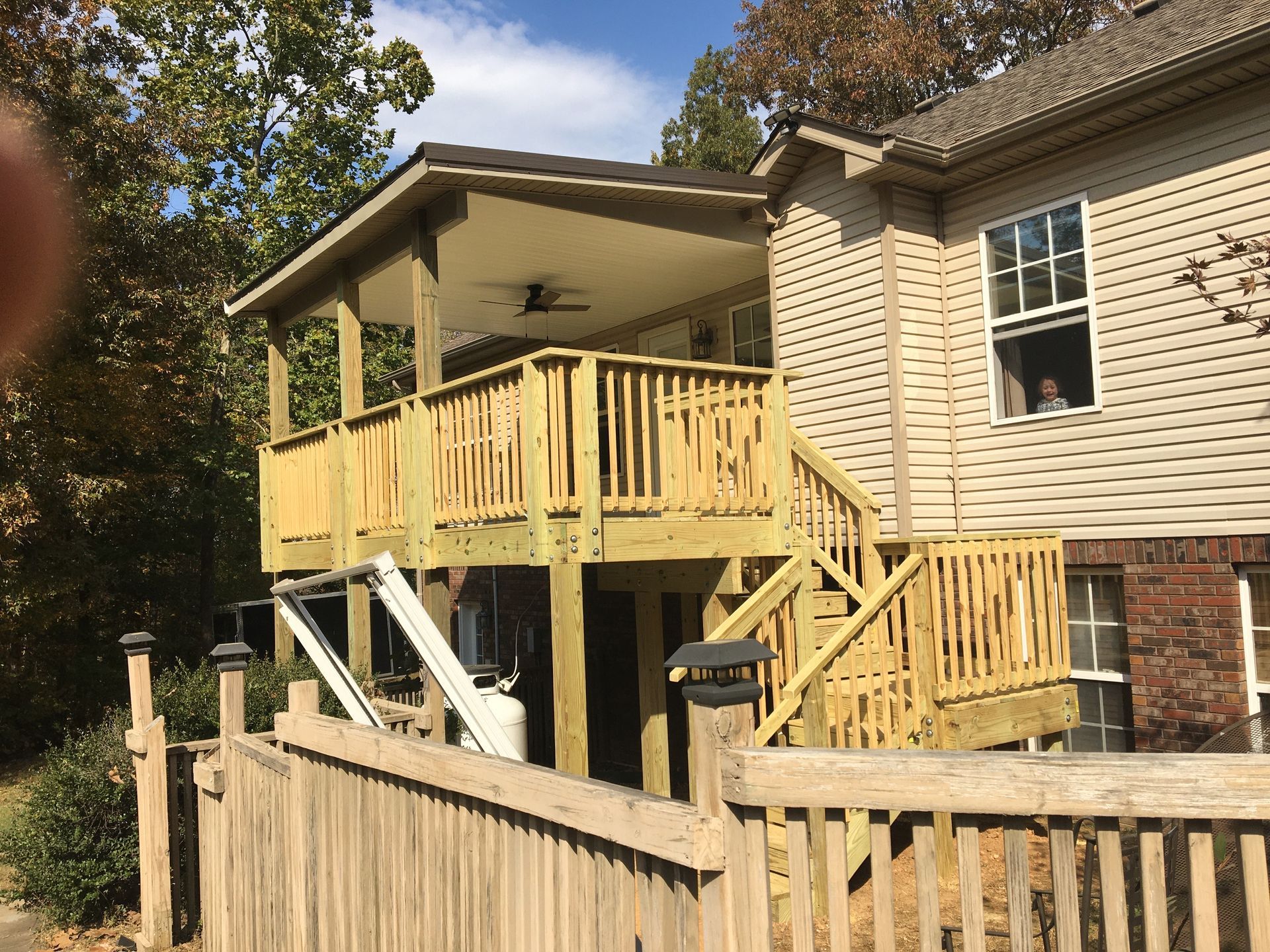 Wooden deck with covered porch attached to a beige house, railing, and a ramp.