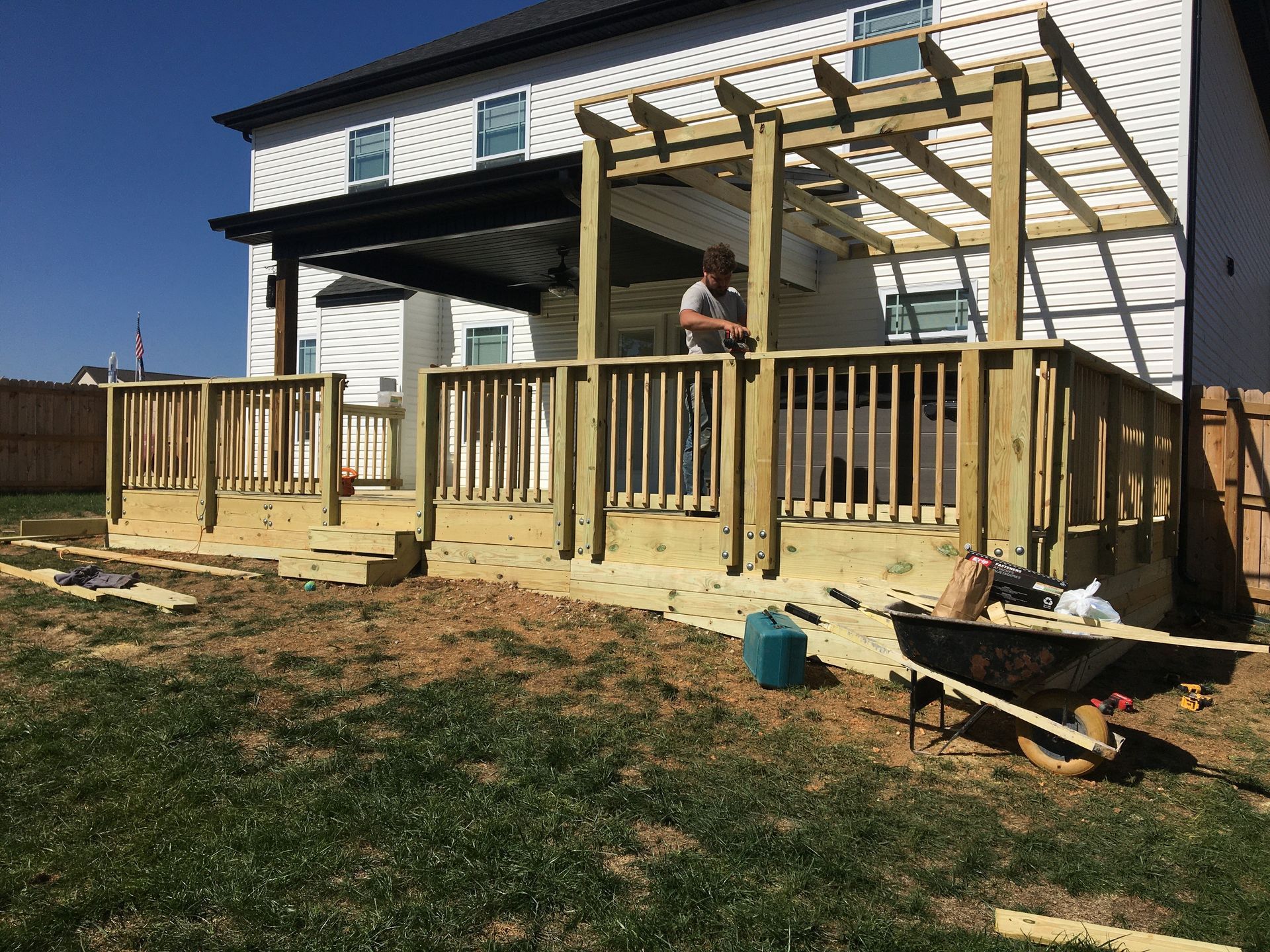 Newly constructed wooden deck with pergola attached to a two-story house, a person is working.