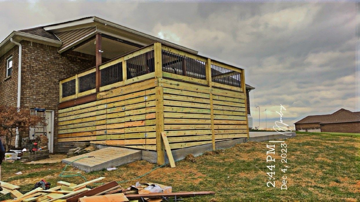A wooden deck under construction attached to a brick house on a cloudy day.