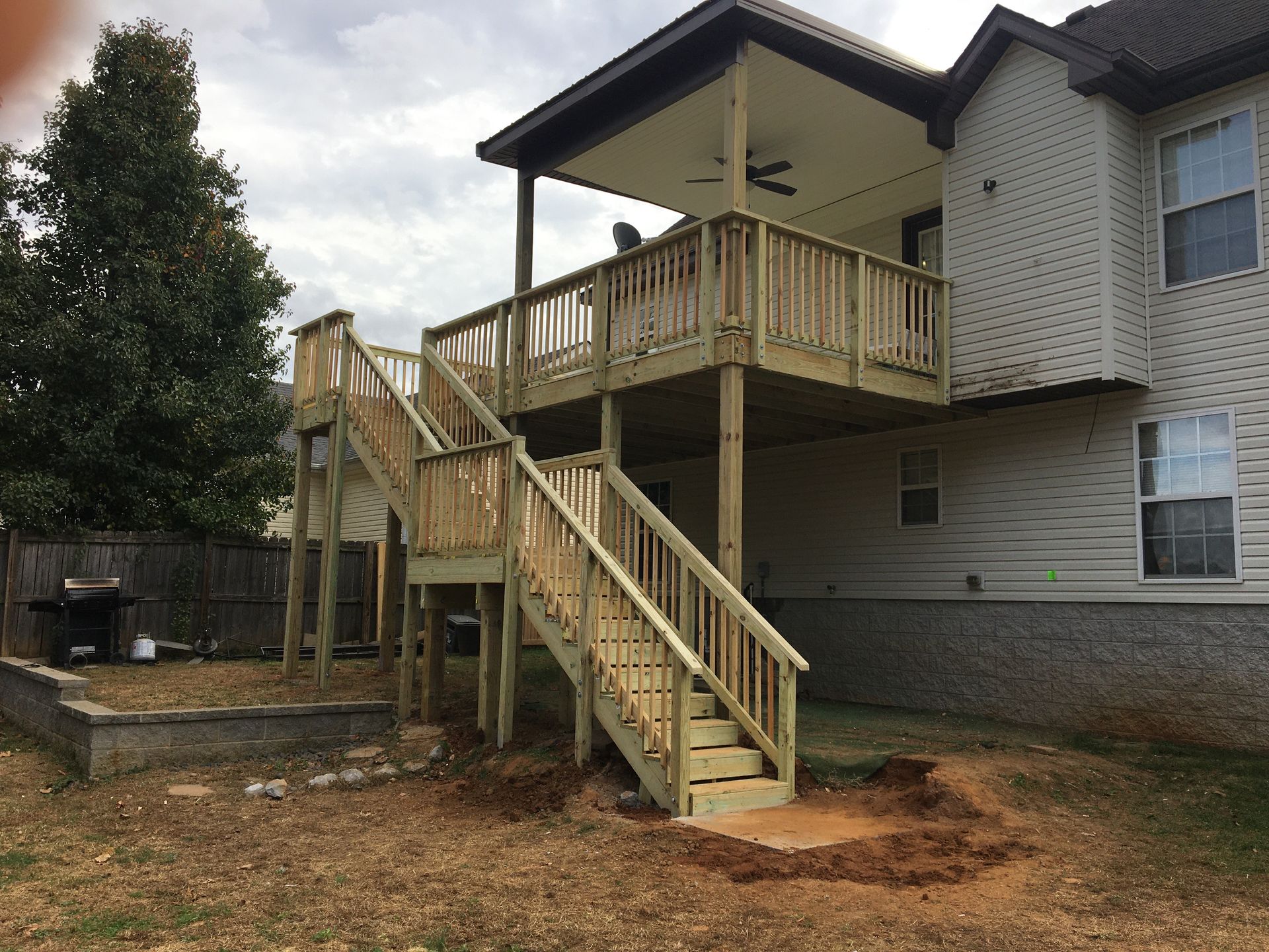 Two-story wooden deck attached to a house. Staircases lead from the deck to the yard.