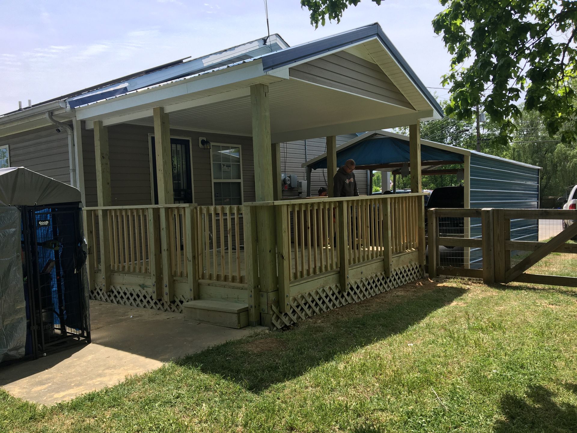 House with a wooden porch and deck, light blue siding, and a detached carport.