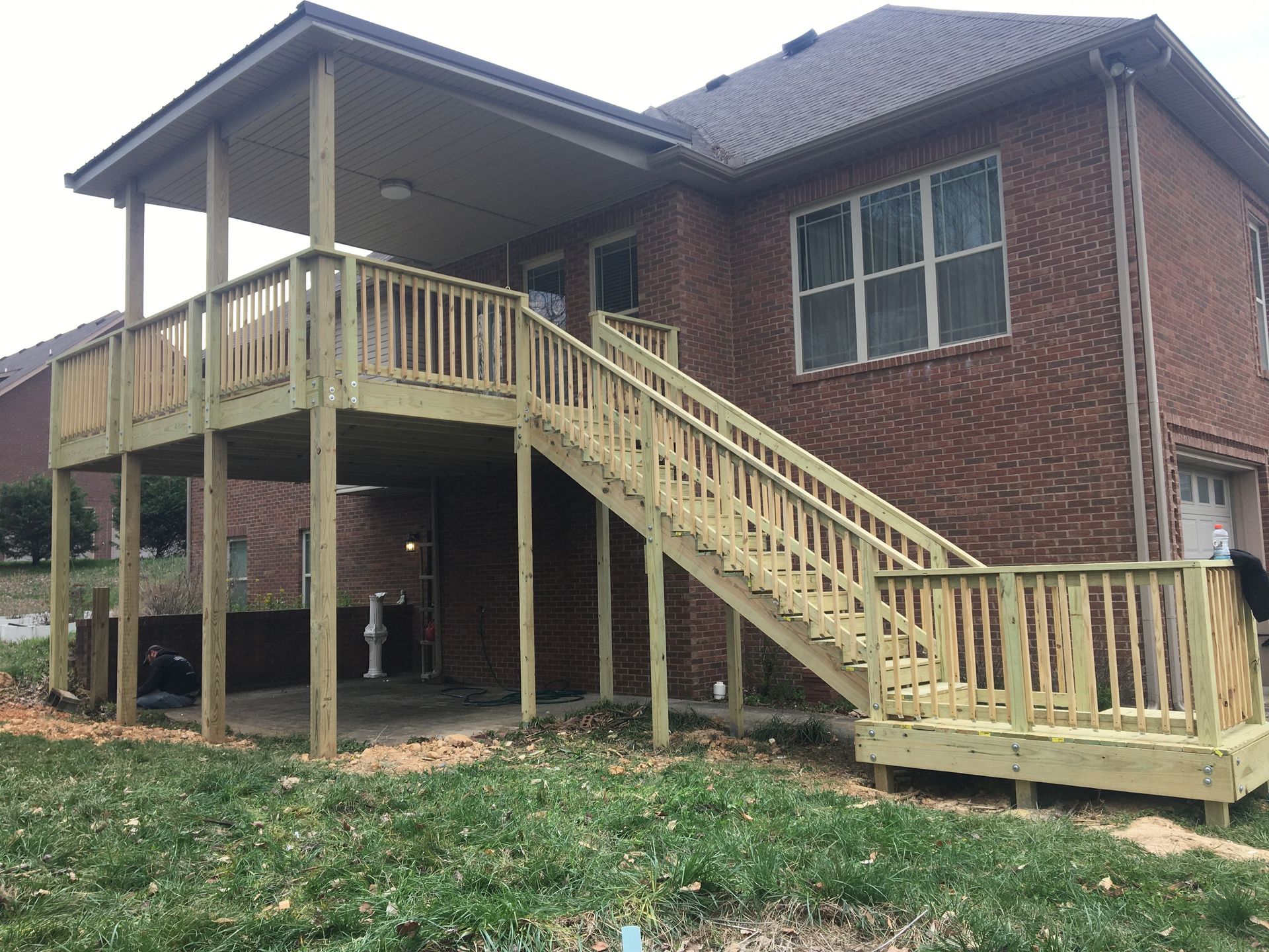 Two-story wooden deck with stairs attached to a brick house. Overhang provides shade.