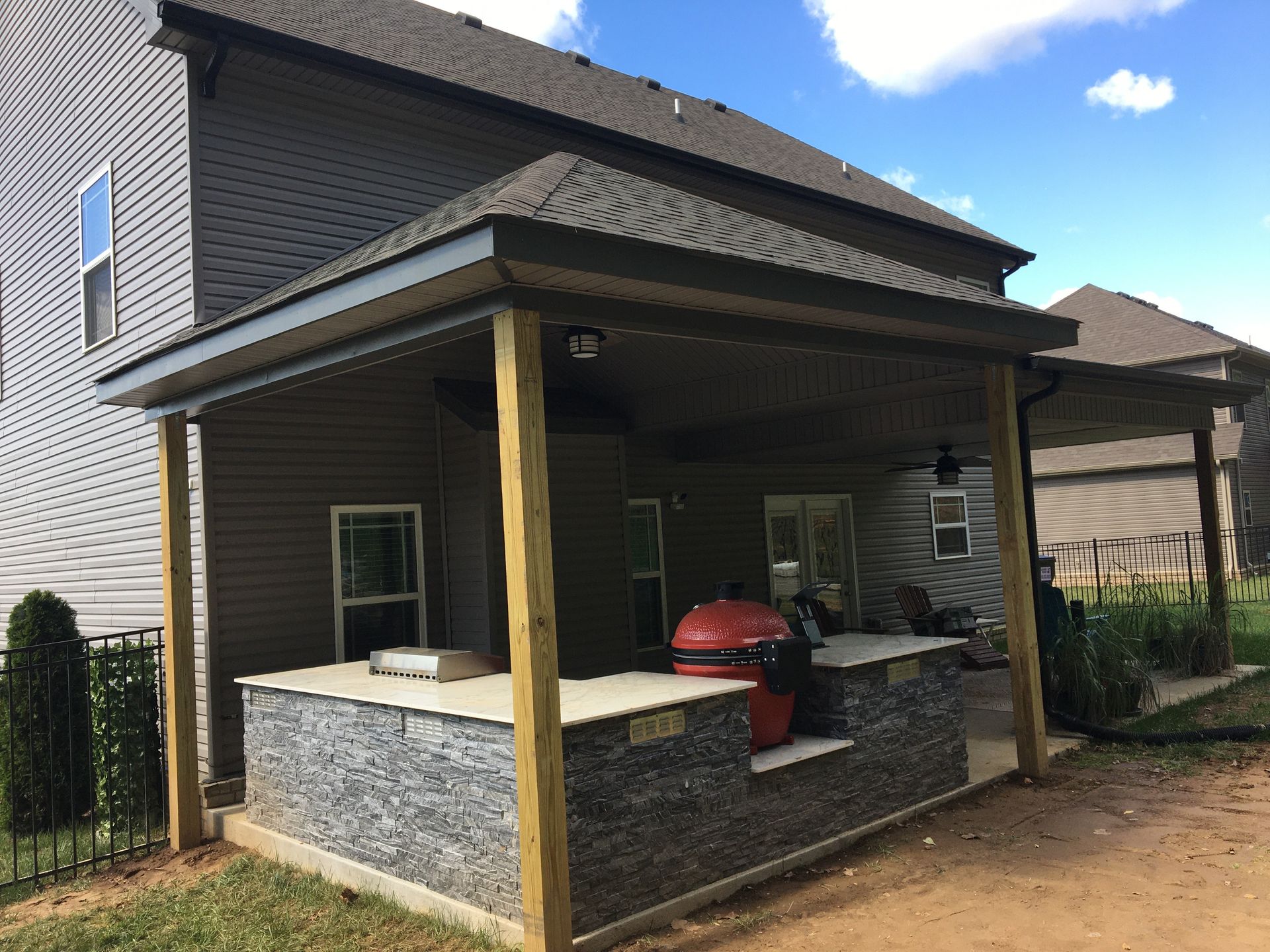 Outdoor kitchen with gray stone base, grill, covered by brown roof.