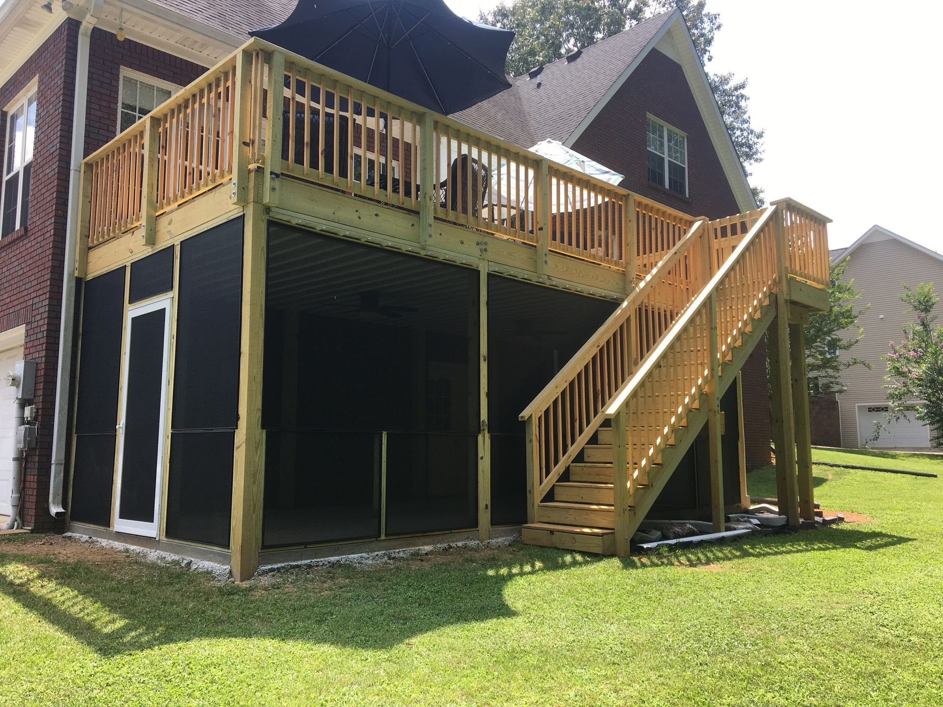 A multi-level wooden deck with stairs attached to a brick house with a screened-in lower level and surrounding green grass.