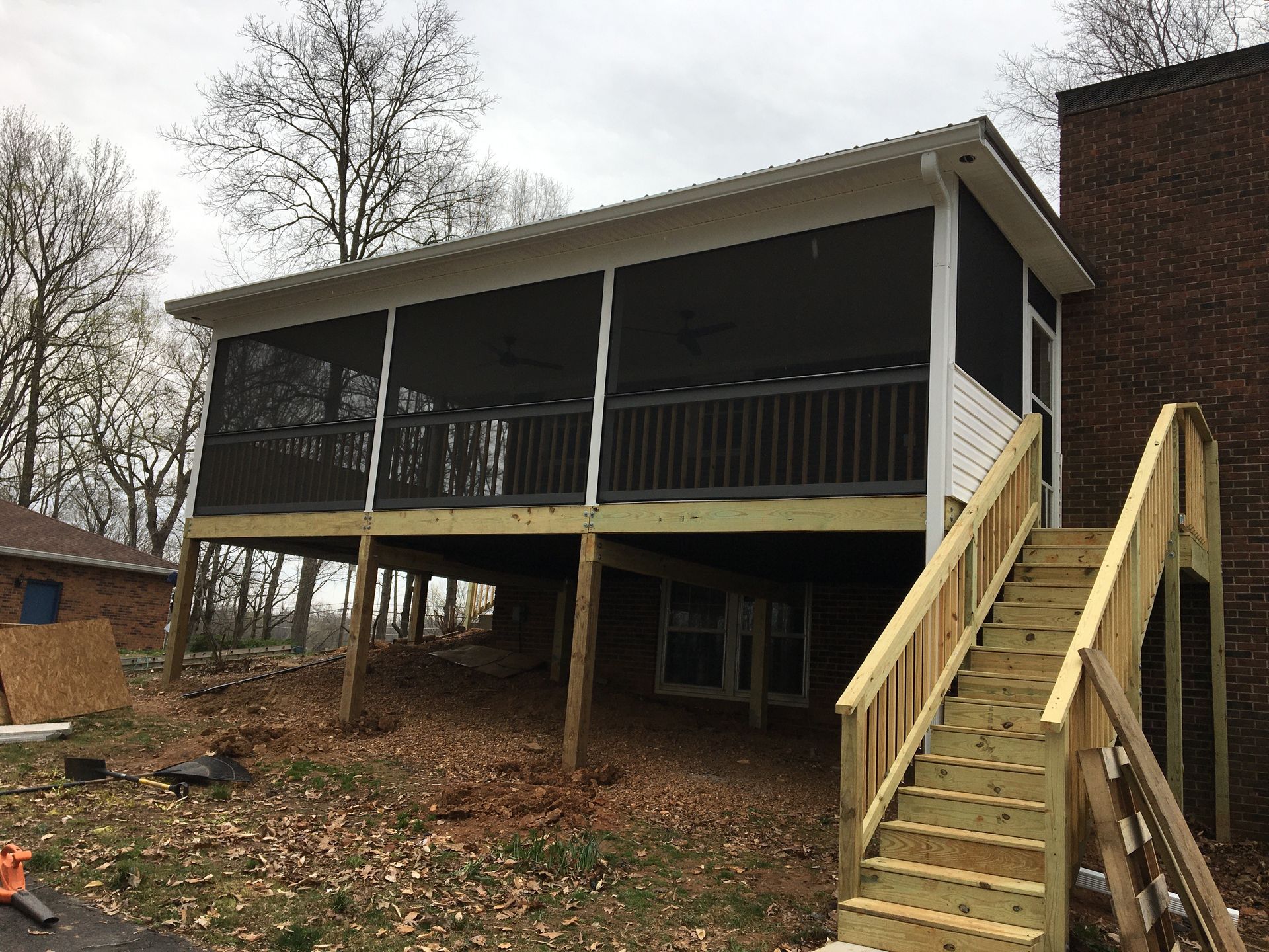Screened porch with wooden deck and staircase attached to a brick chimney and house exterior.