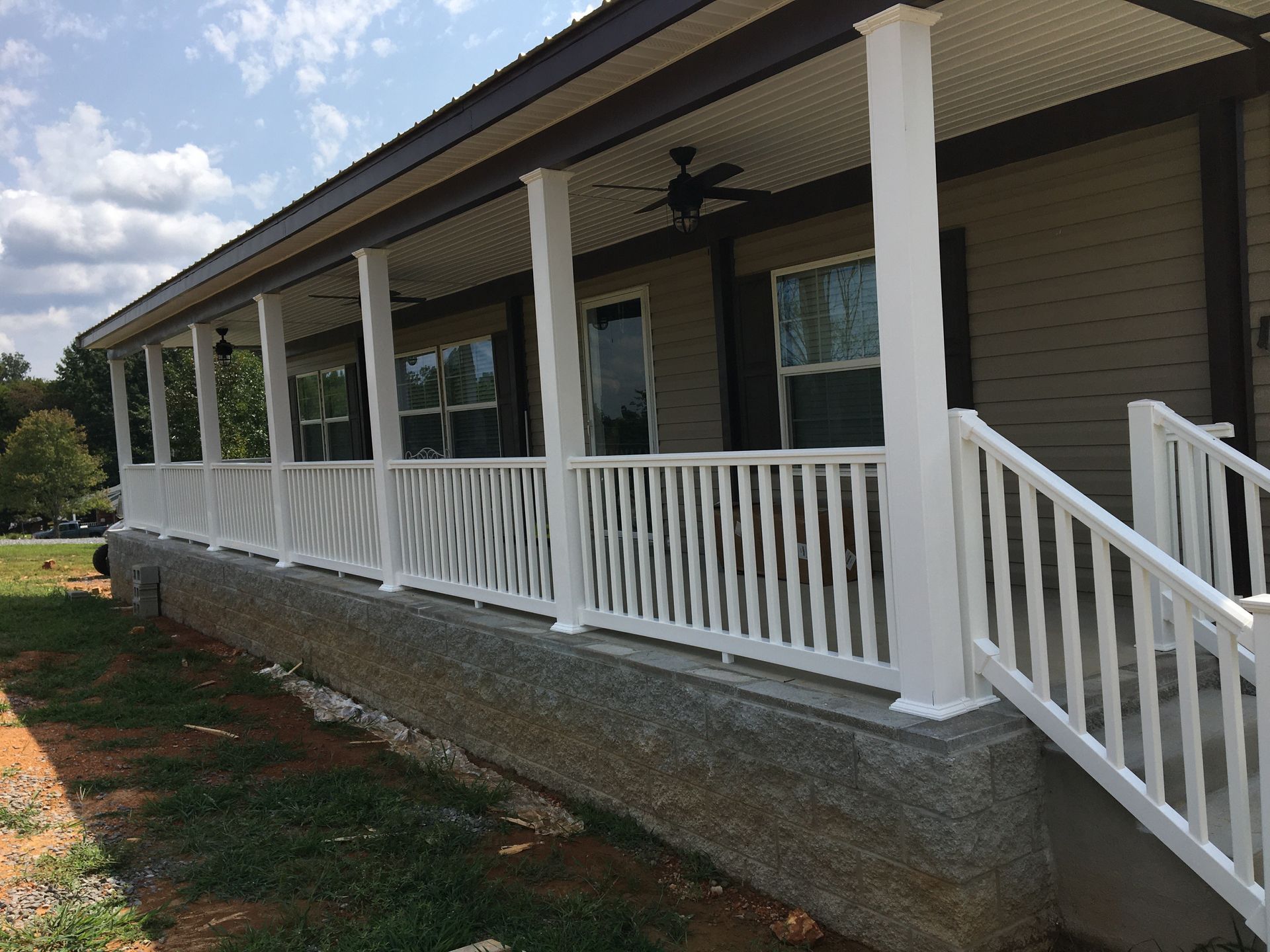 White porch with railing and columns on a beige house under a blue sky.