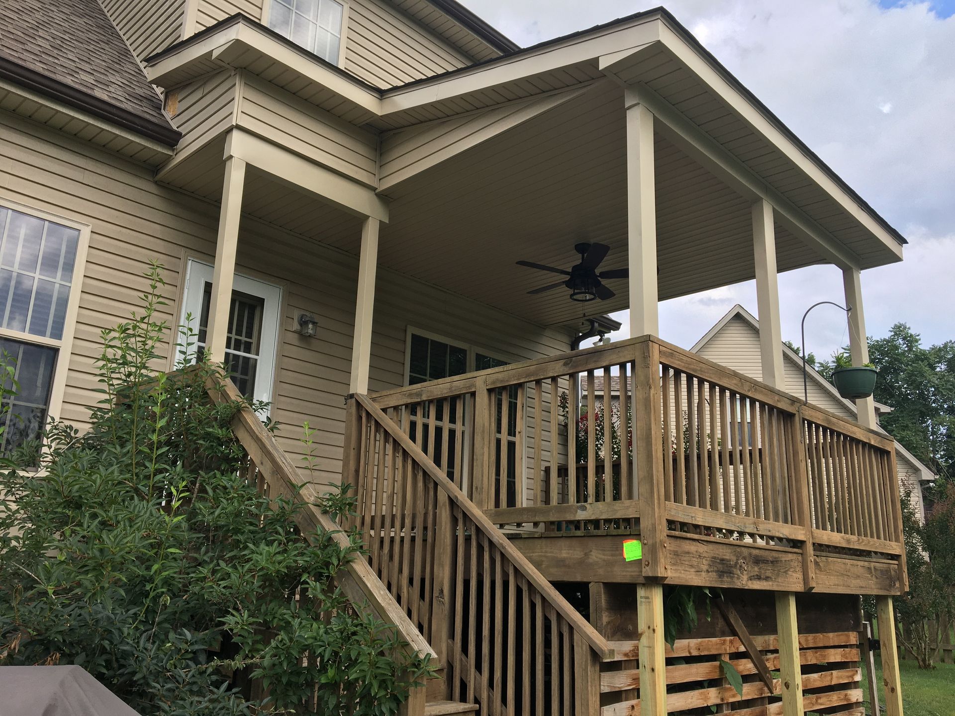 A wooden deck with stairs and a covered porch attached to a beige house.