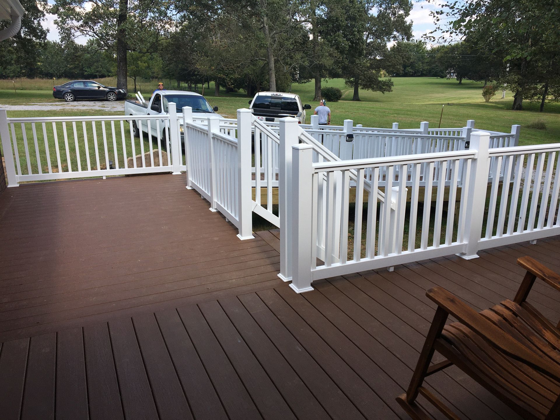 White fenced deck with brown composite decking. A wheelchair lift. Trucks in background.