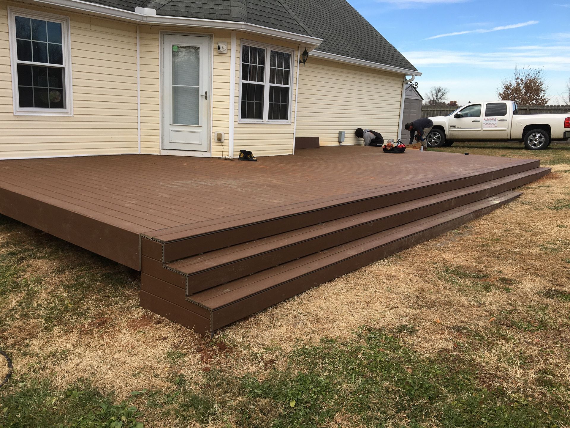 Brown composite deck with steps attached to a light-colored house.