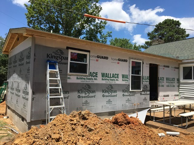 Exterior of a building under construction. Studs, windows, and weatherproofing visible; ladder leans against the wall.