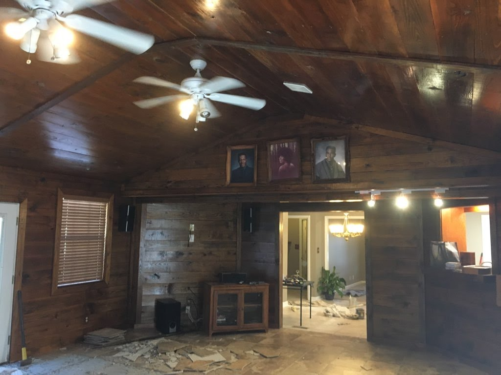 Wooden-paneled room with three portraits, two ceiling fans, and a glimpse into another room.