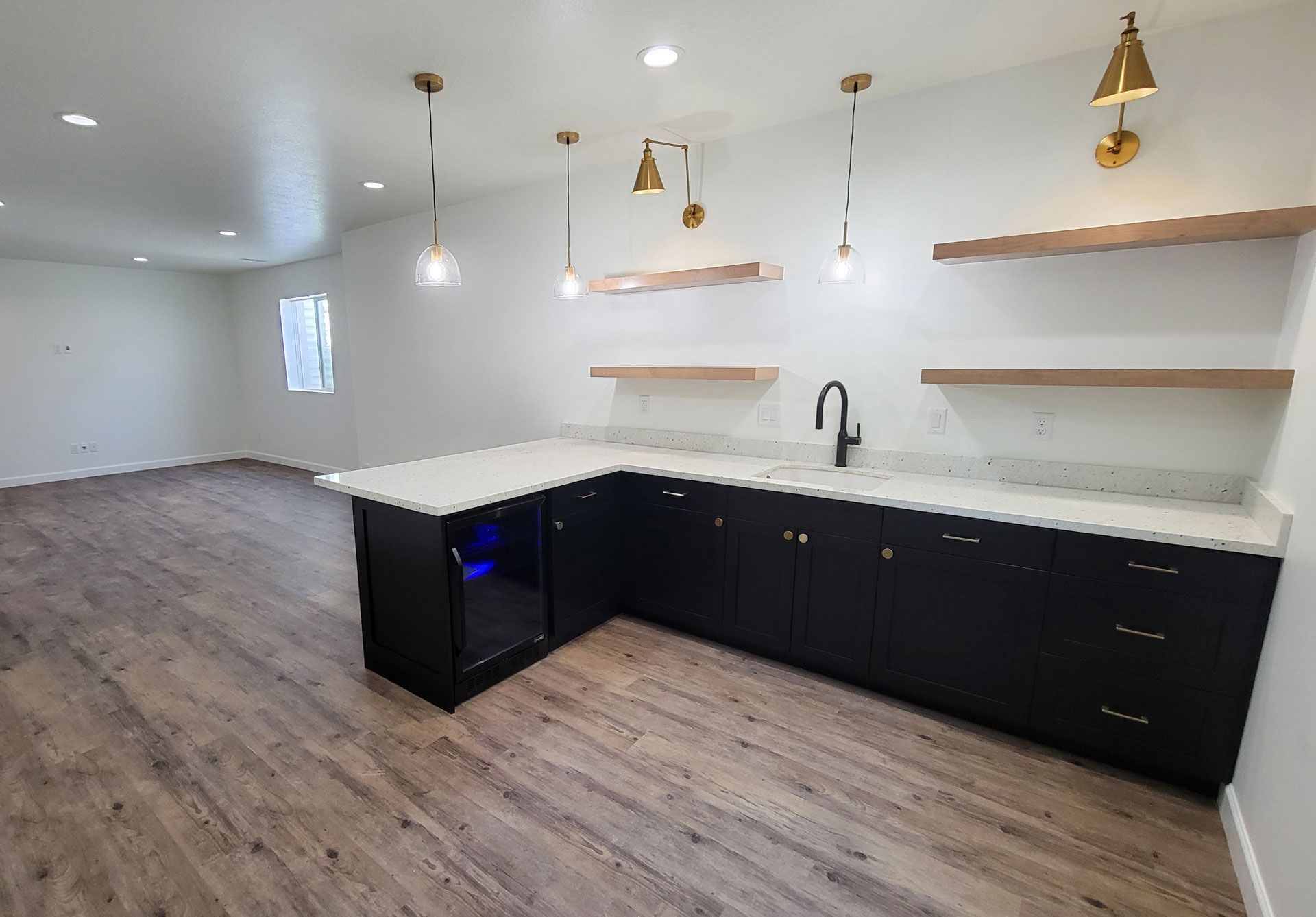 A kitchen with black cabinets , white counter tops , and wooden floors.