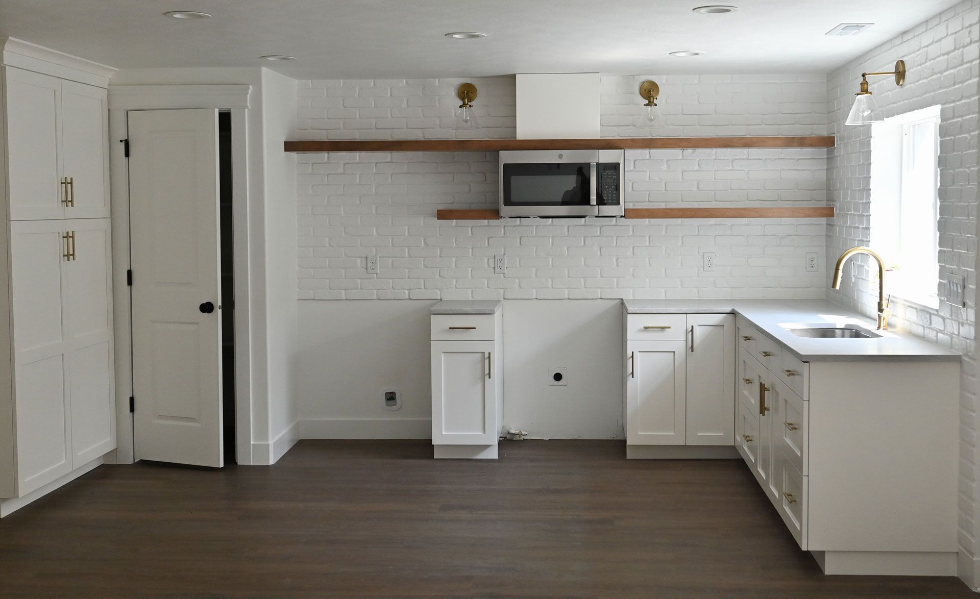 An empty kitchen with white cabinets , a sink , and a microwave.