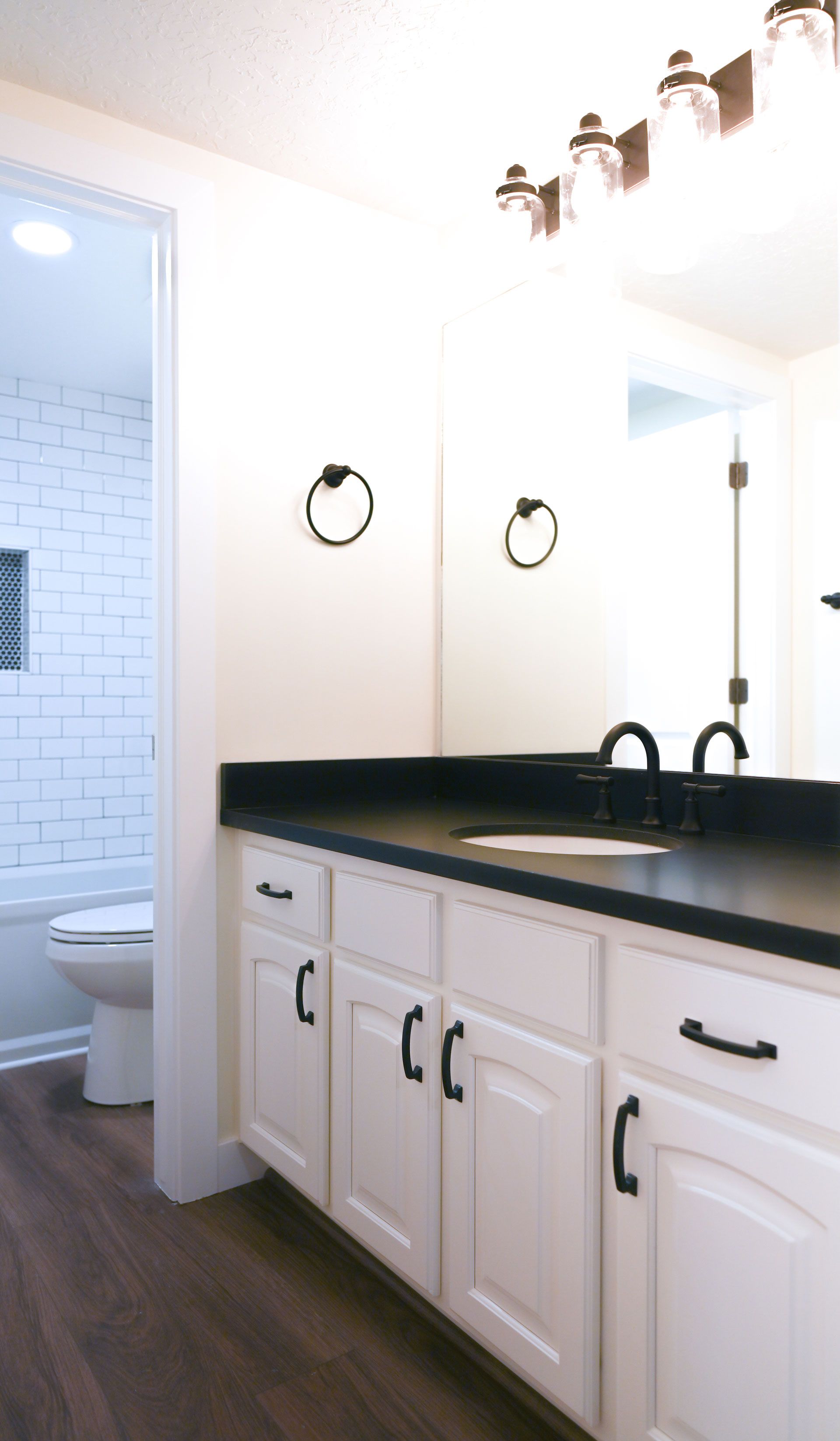 A bathroom with white cabinets , black counter tops , a toilet and a sink.