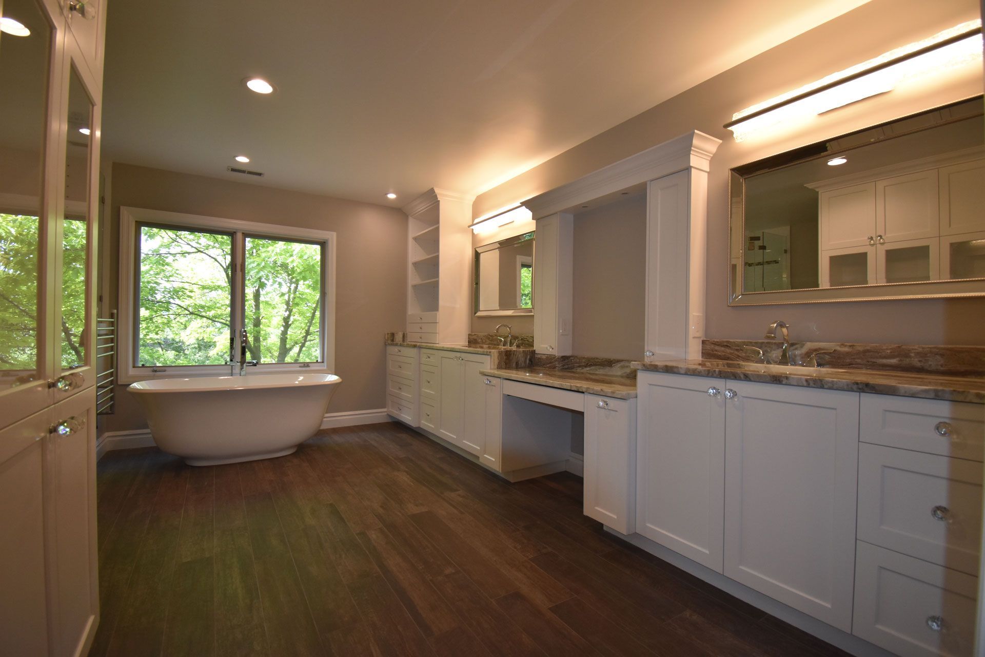 A bathroom with a tub , sinks , mirrors and a large window.