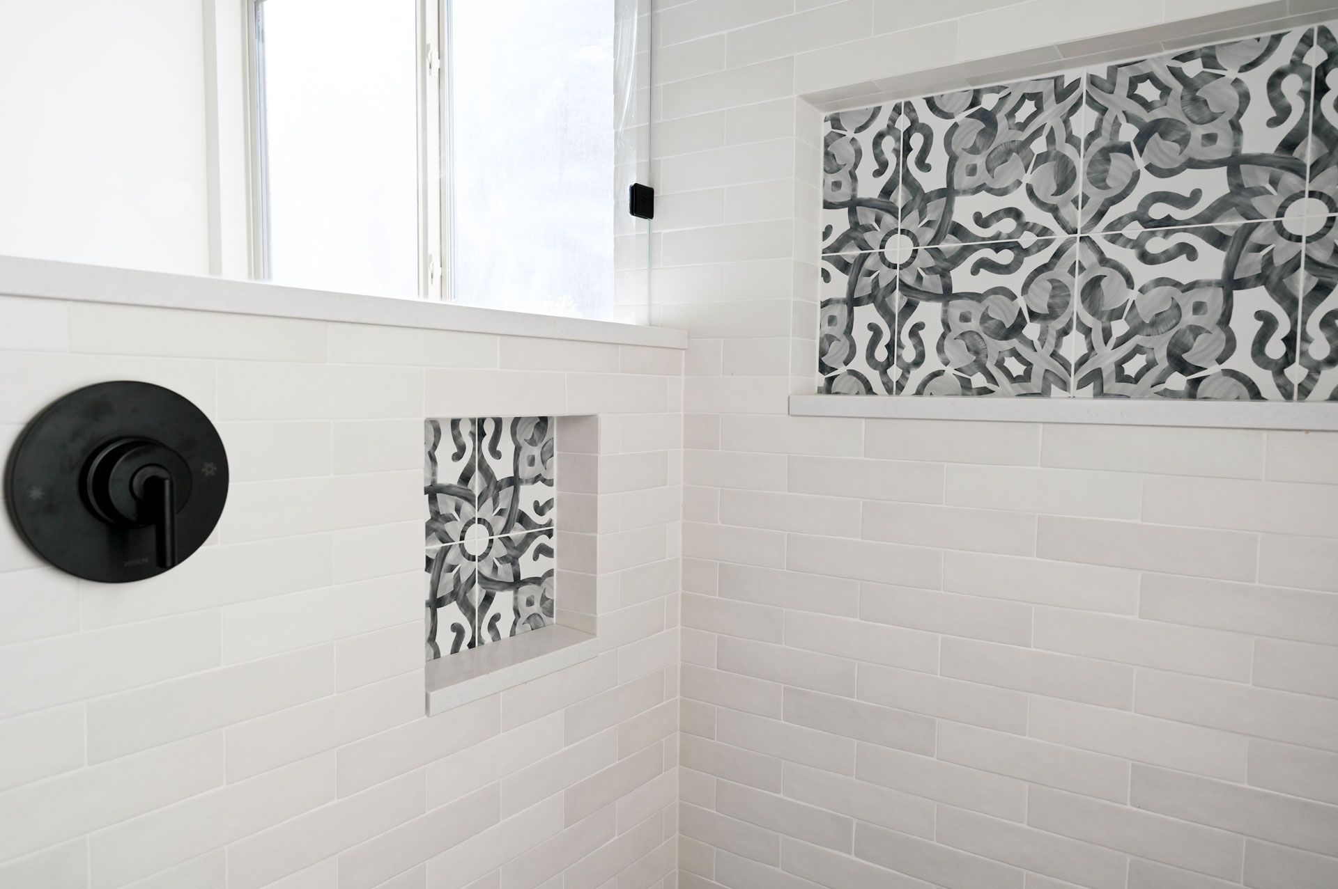 A bathroom with white tiles and a black shower head.