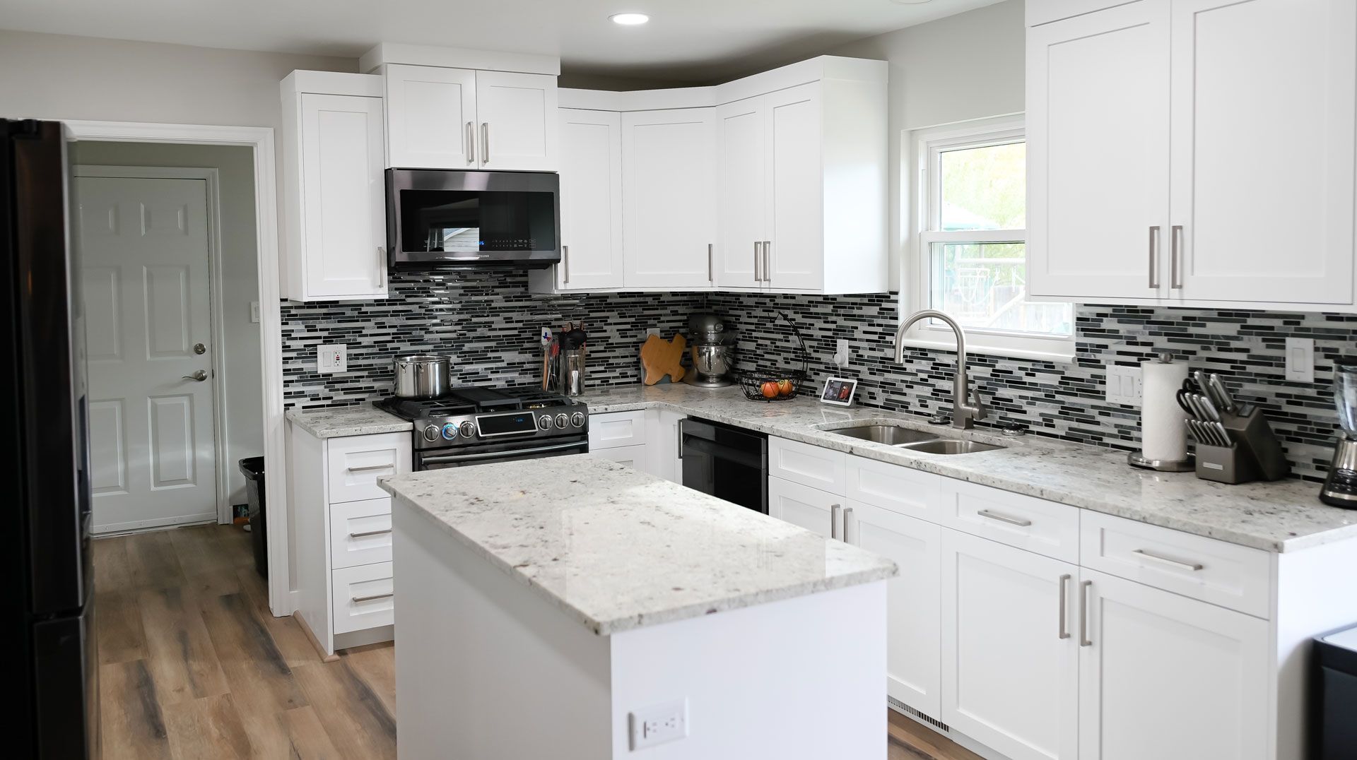 A kitchen with white cabinets , granite counter tops , stainless steel appliances and a large island.