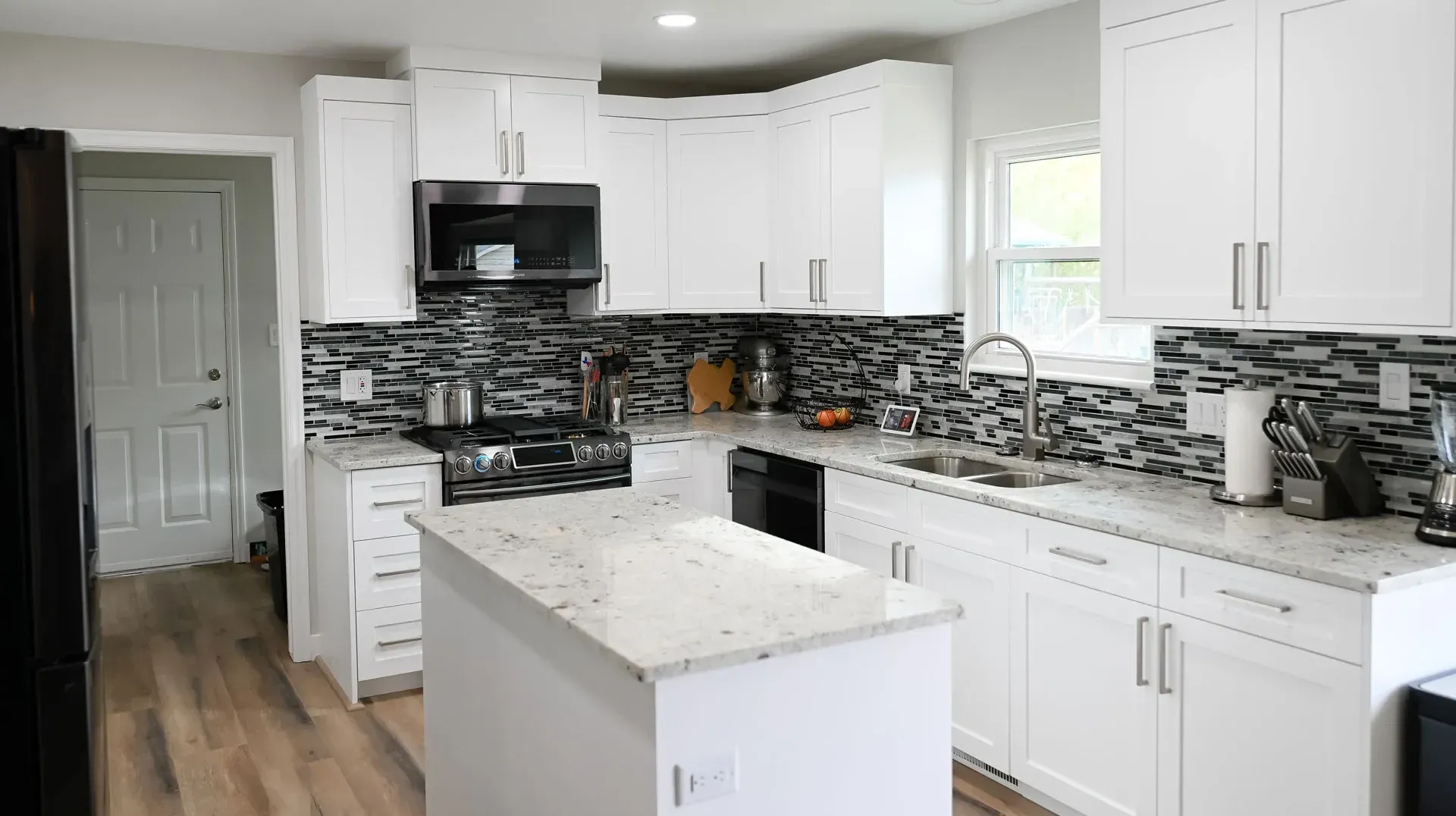A kitchen with white cabinets , granite counter tops , stainless steel appliances and a large island.