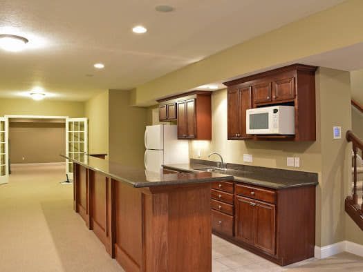 A kitchen with wooden cabinets , a refrigerator , a microwave and a bar.