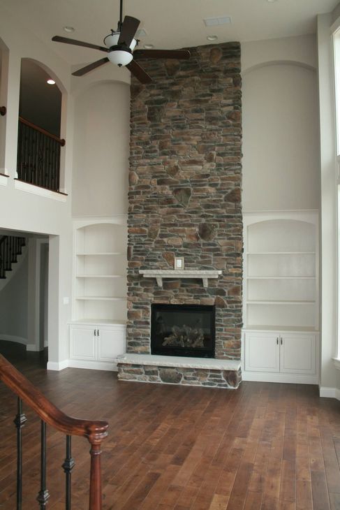 A living room with a stone fireplace and a ceiling fan