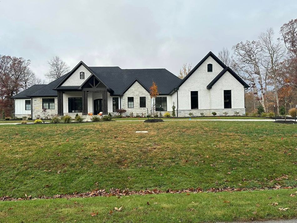 A large white house with a black roof is sitting on top of a lush green field.