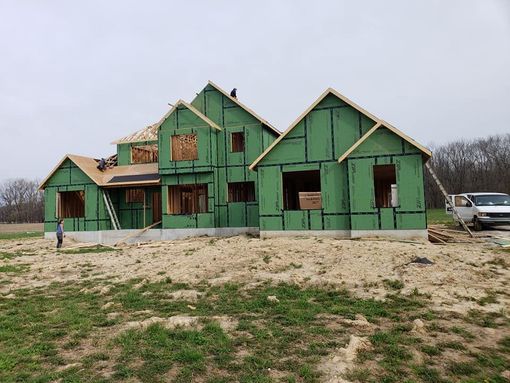 A large house is being built in a field with green siding.