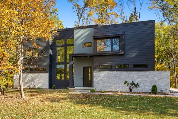 A kitchen with wooden cabinets , a refrigerator , a microwave and a bar.