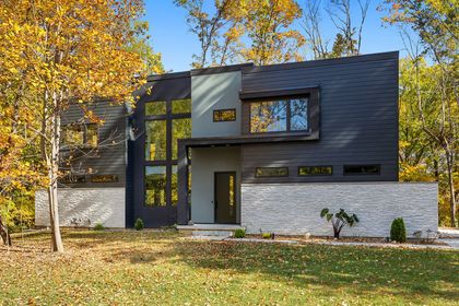 Modern two-story house with dark siding, white stone accents, and autumn trees in front