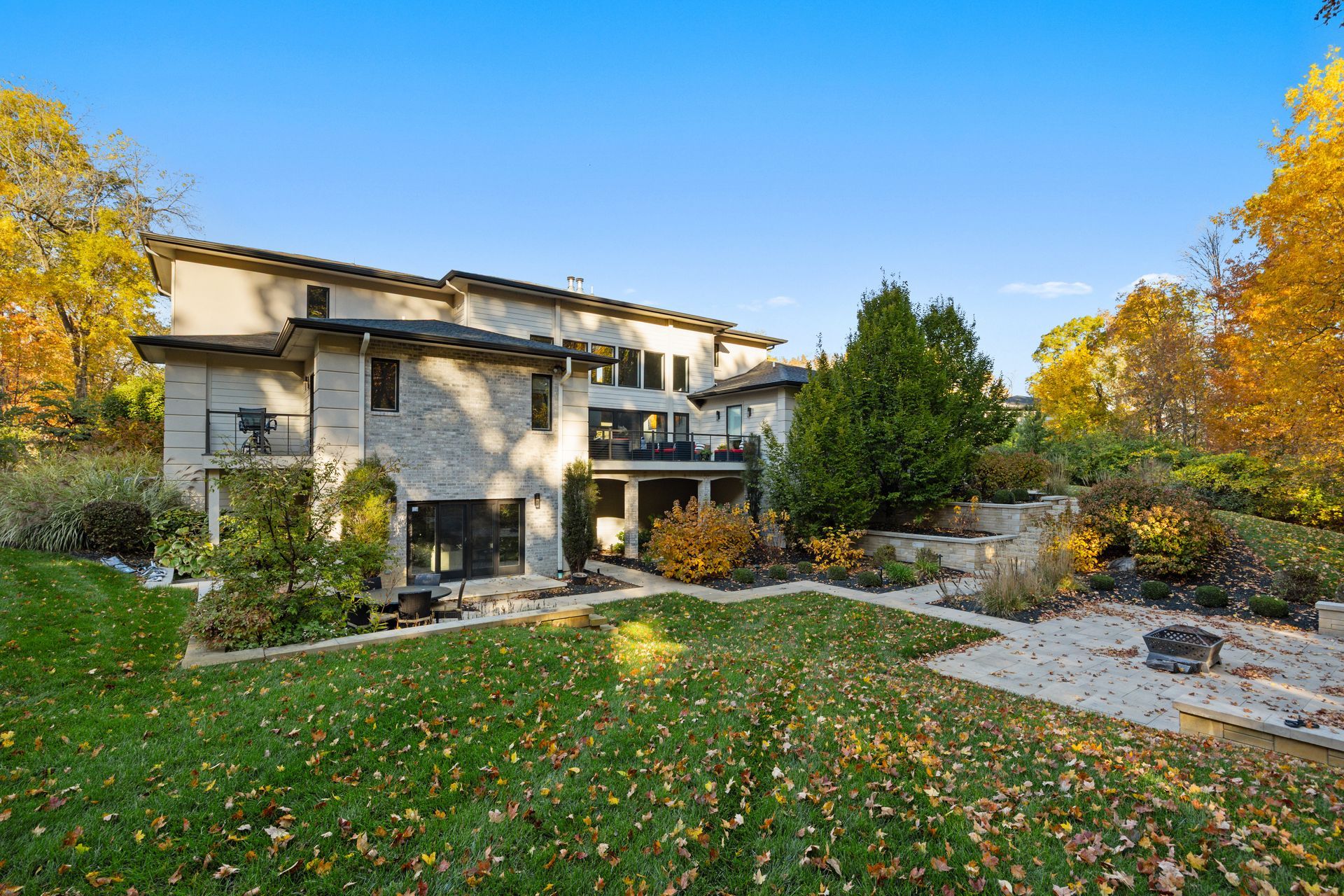 A large brick house with a gray roof is sitting on top of a lush green field.