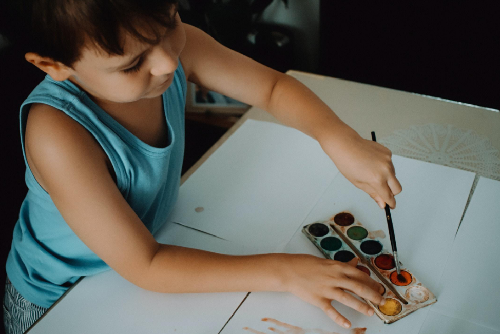 A young boy is sitting at a table painting with watercolors.