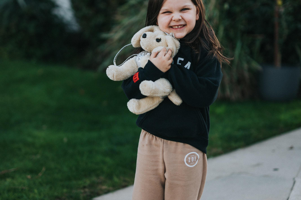 A little girl is holding a stuffed dog on a leash.