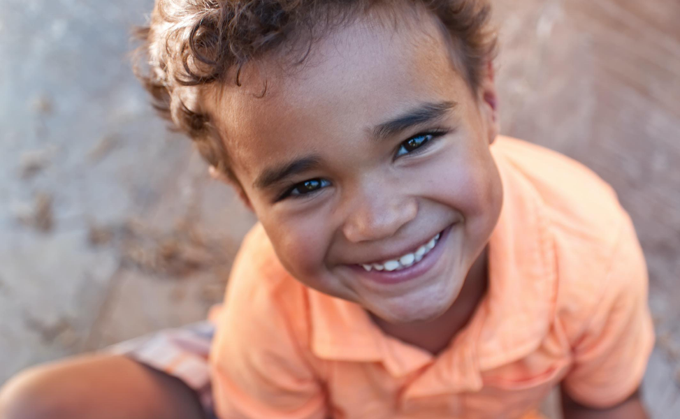 A young boy is smiling for the camera while sitting on the ground.