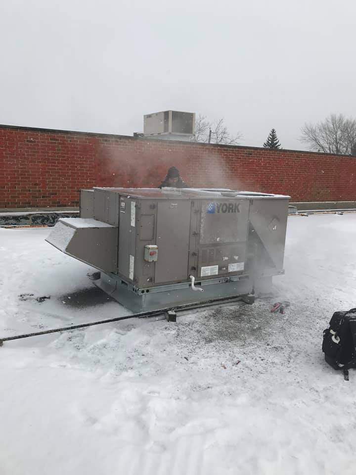 Un grand climatiseur est posé au sommet d’un toit enneigé.