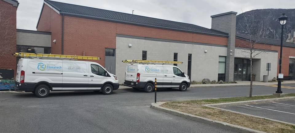 Deux camionnettes blanches sont garées devant un immeuble.