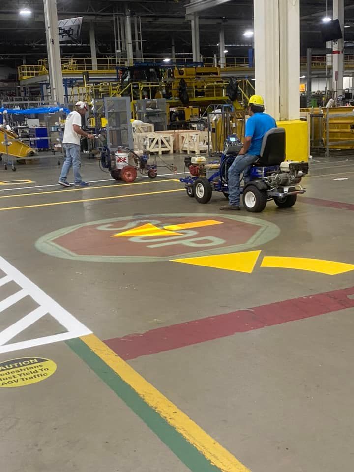 A man is riding a lawn mower in a warehouse with a stop sign painted on the floor